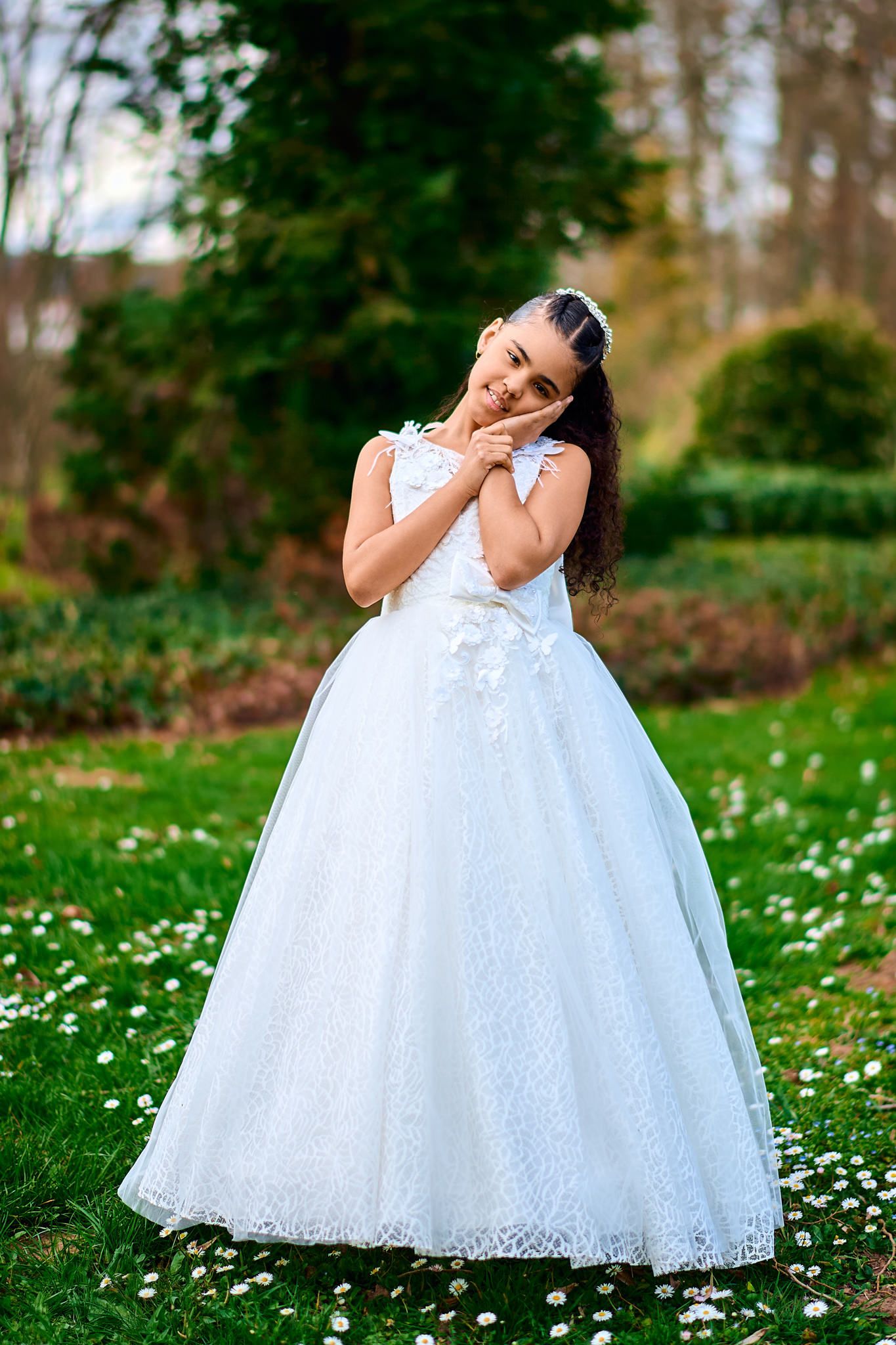 White lace dress twirls gracefully in a garden setting with scattered white flowers on green grass.