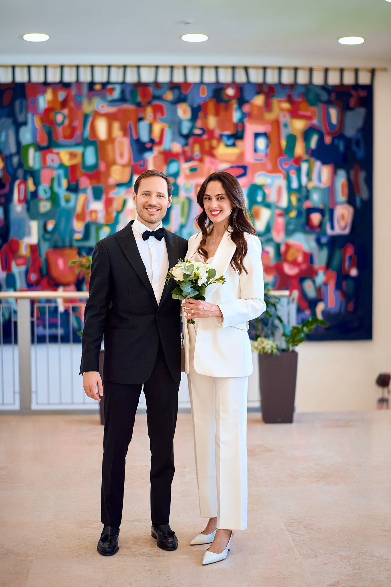 Wedding couple and attendants pose in formal attire against vibrant blue and red abstract art backdrop.