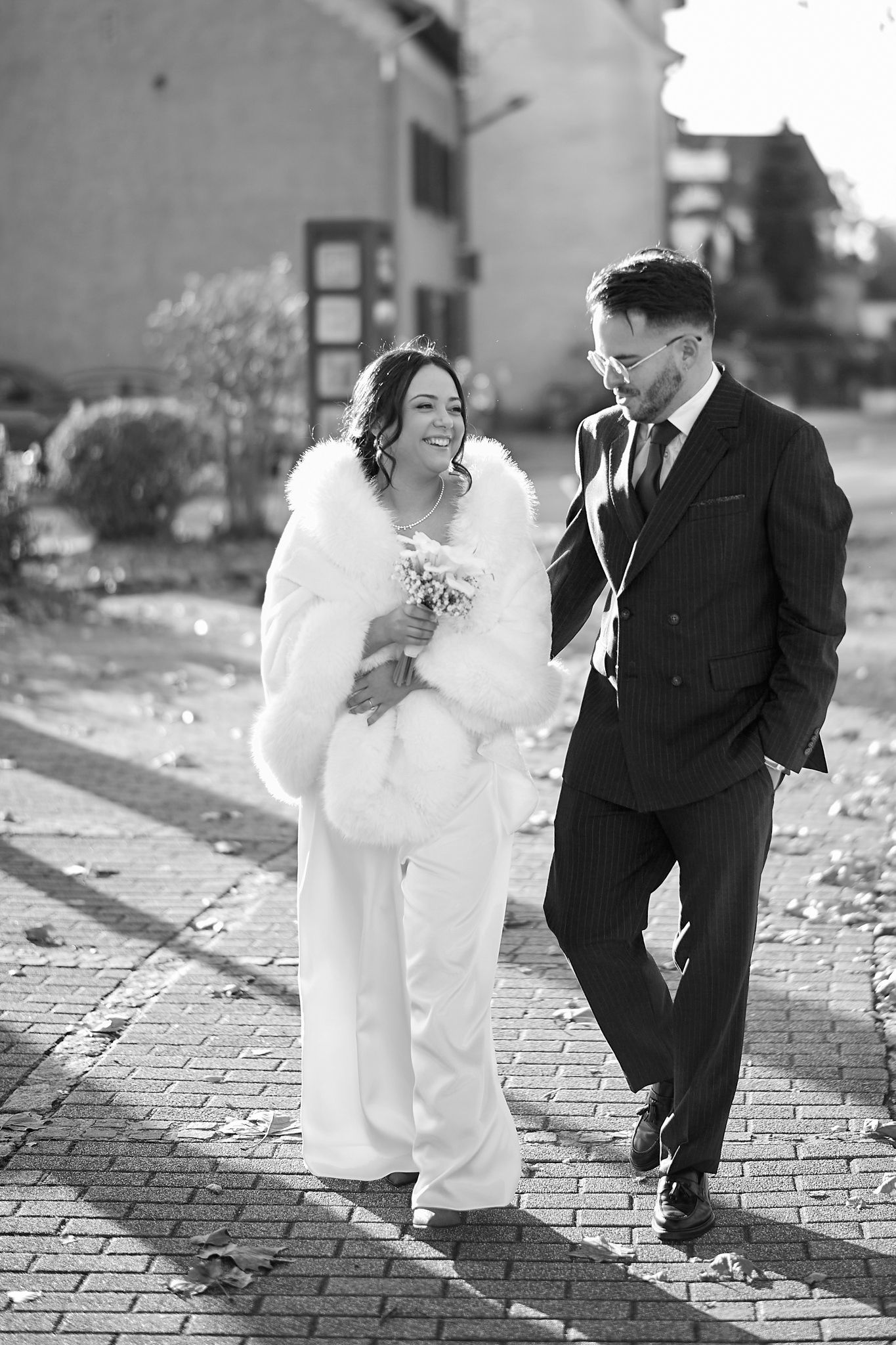 Black and white wedding photos showing playful interactions between a couple on cobblestone pavement.