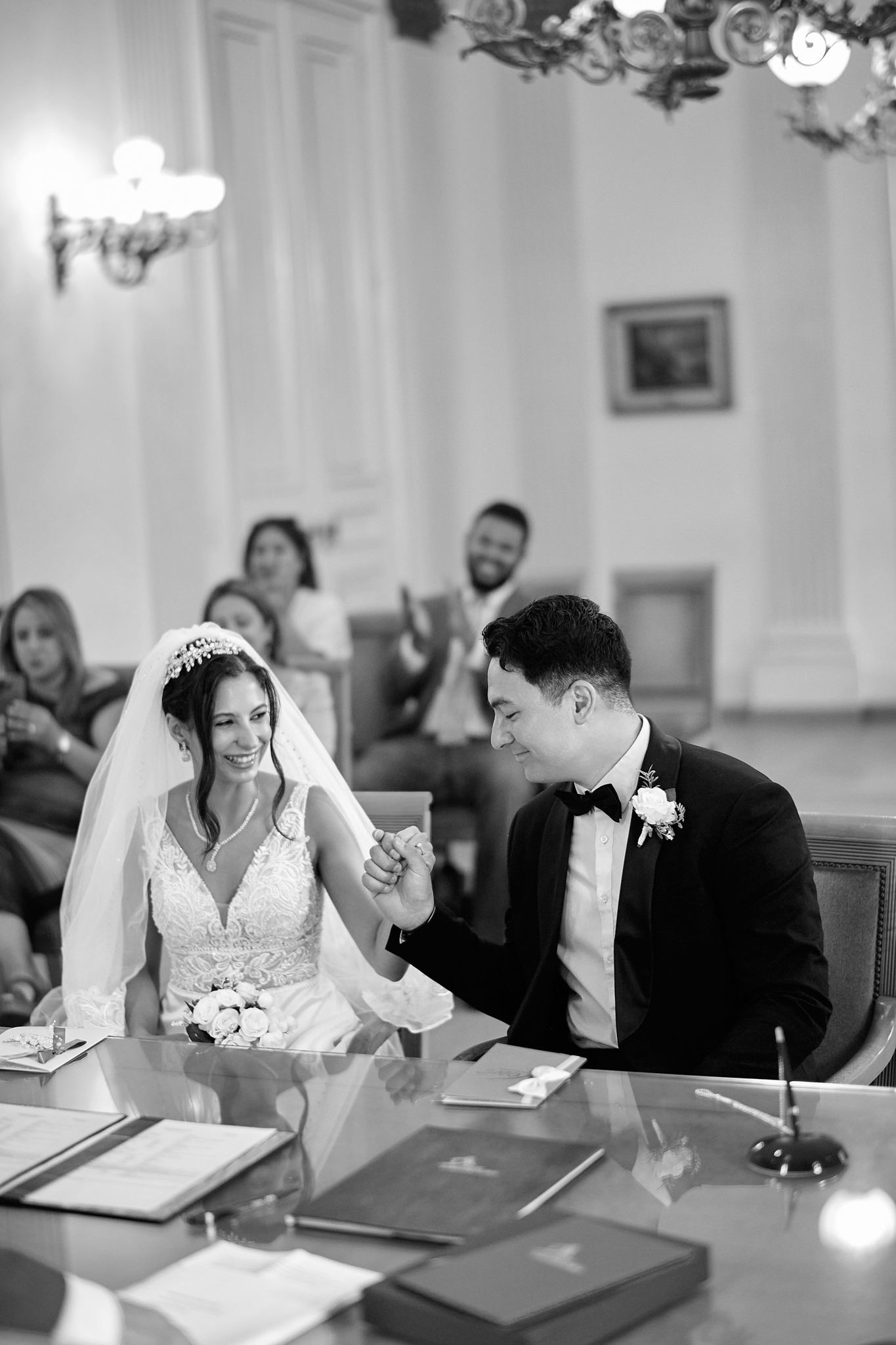 Wedding couple signs marriage documents at a table with chandelier overhead.