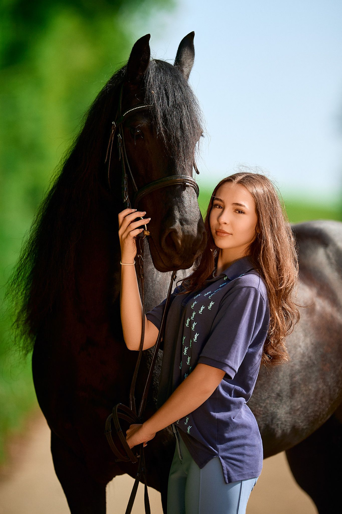 Person in navy shirt embracing black horse outdoors with natural greenery background.