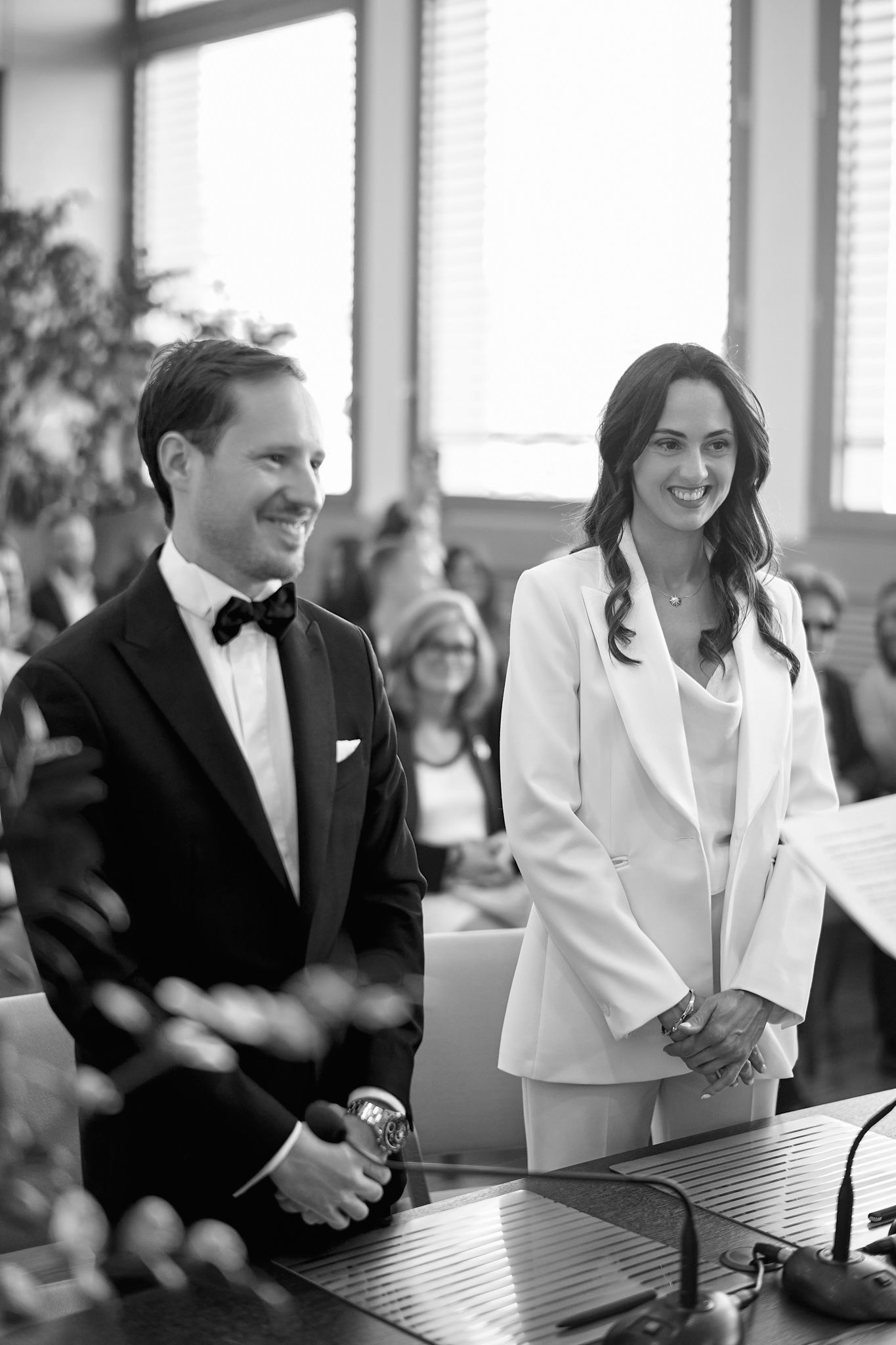 A couple shares laughter during their wedding ceremony while seated at a table in formal attire.