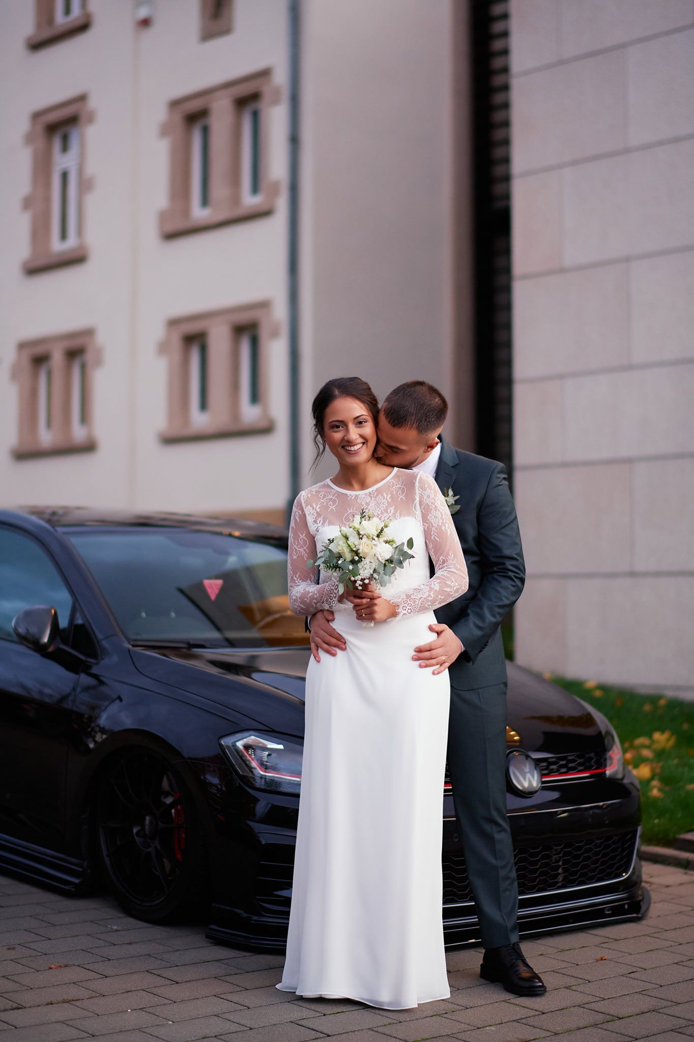 Romantic moment between newlyweds by a car on their wedding day.