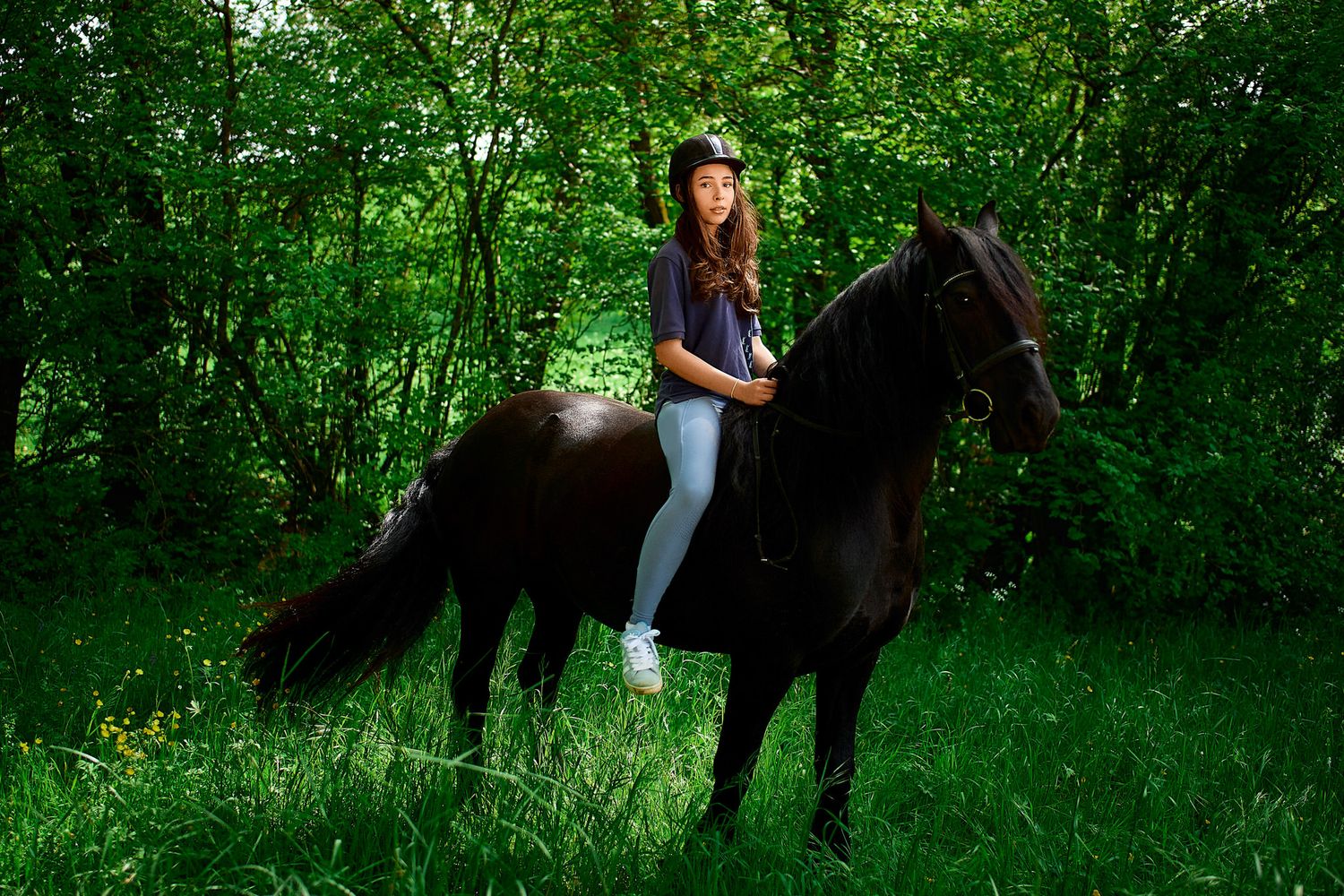 Horses and handlers walk along a lush green forest path.