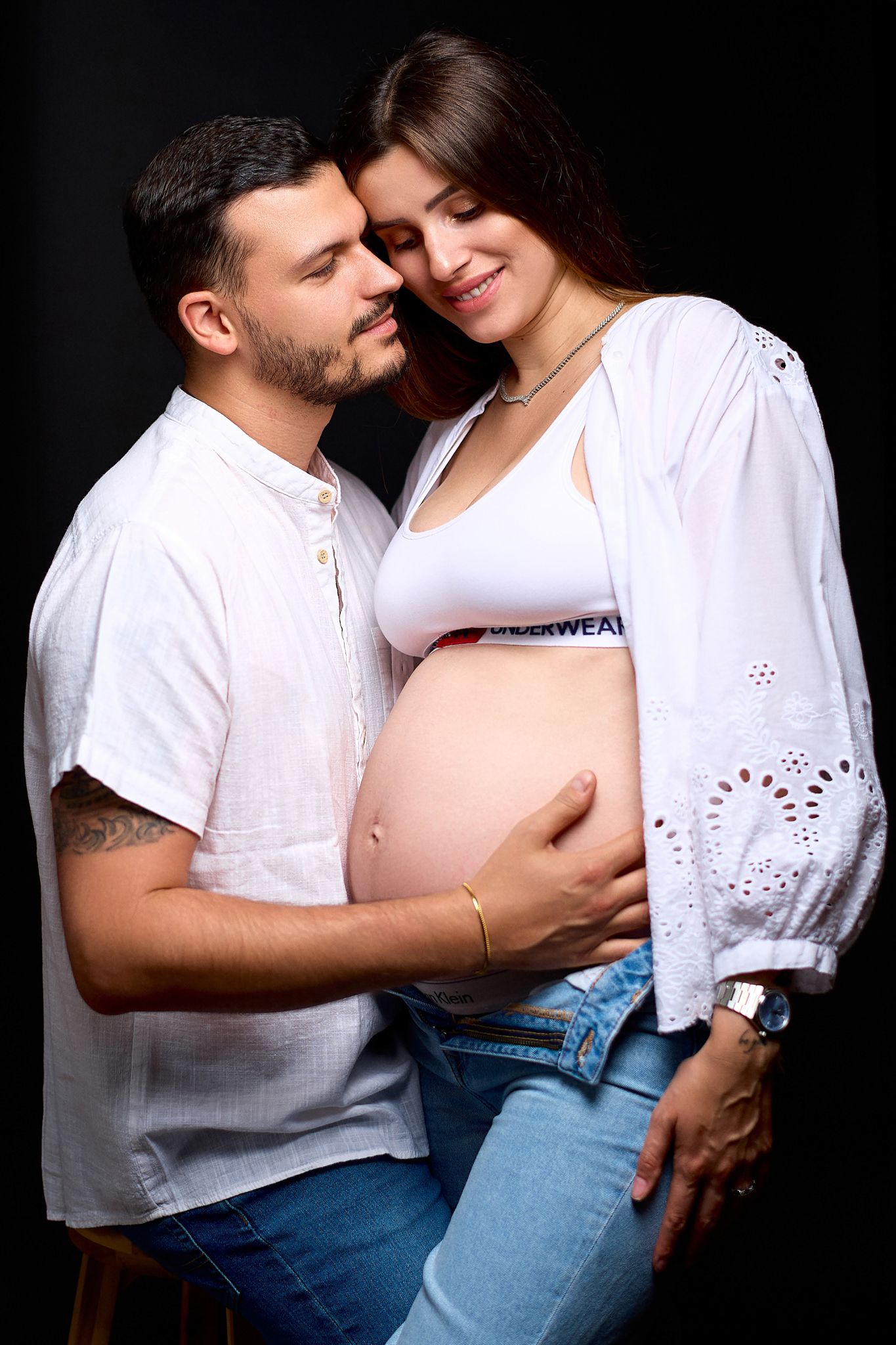 Intimate couple's photo session against black background wearing white and denim.