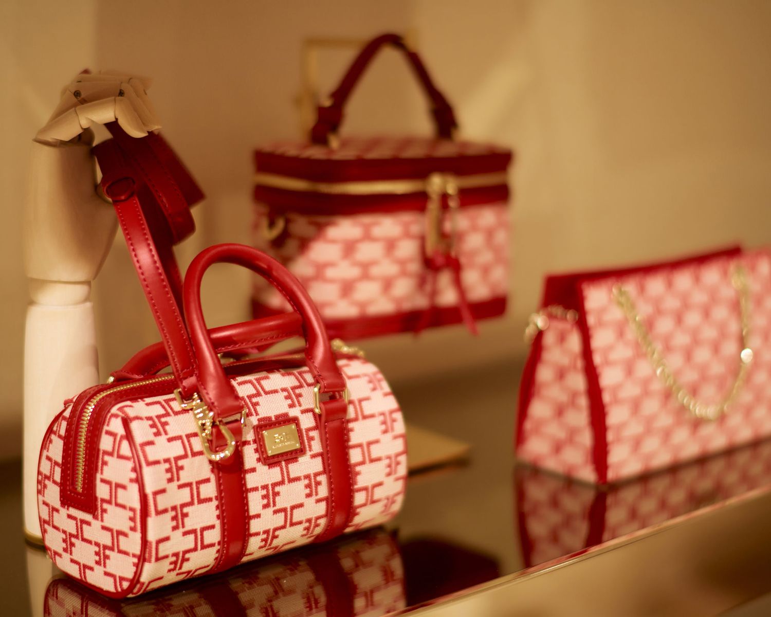 Row of pink and red designer handbags displayed on a shelf.