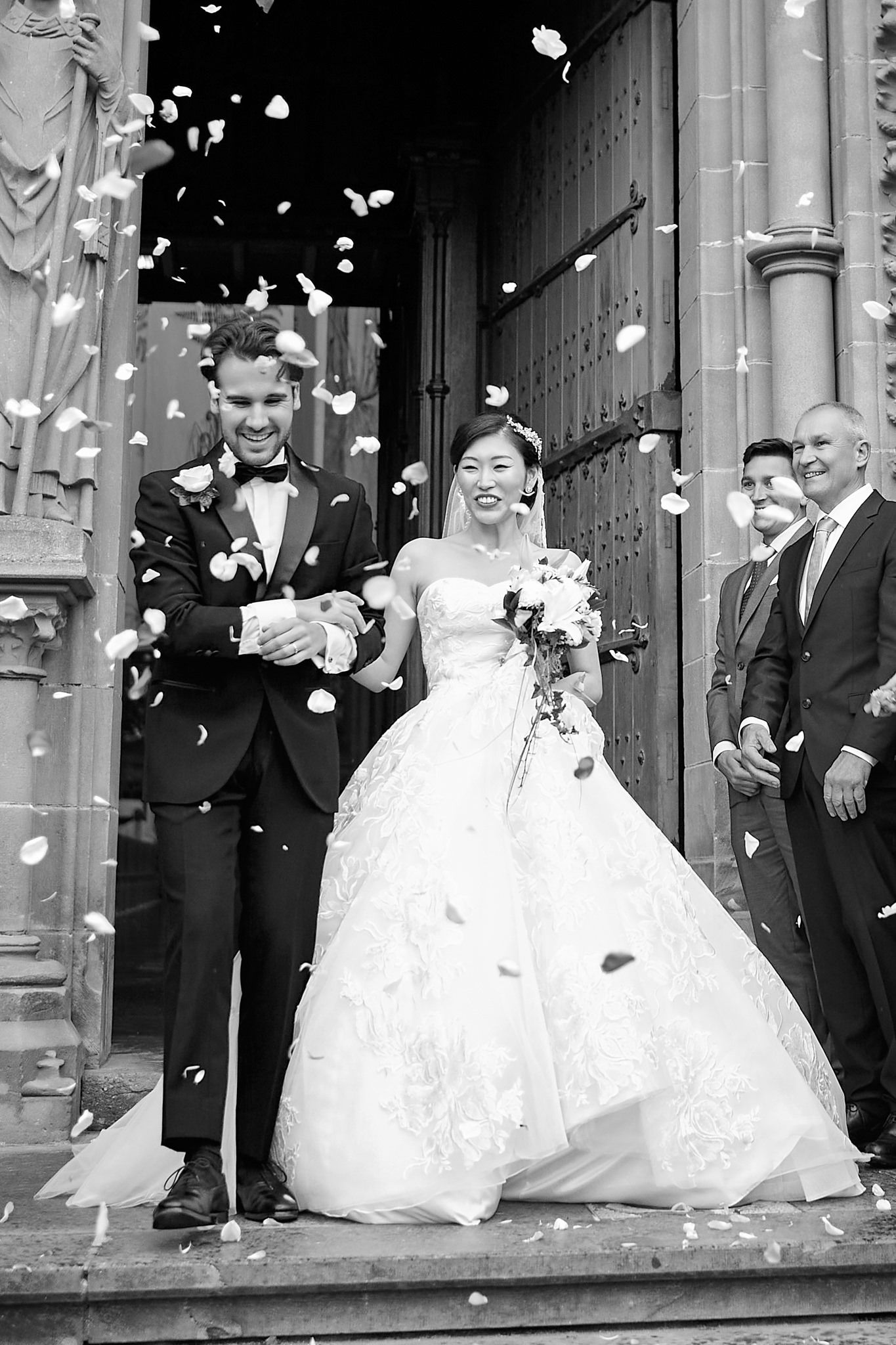 Wedding celebration outside historic building with flower petals being tossed in celebration.
