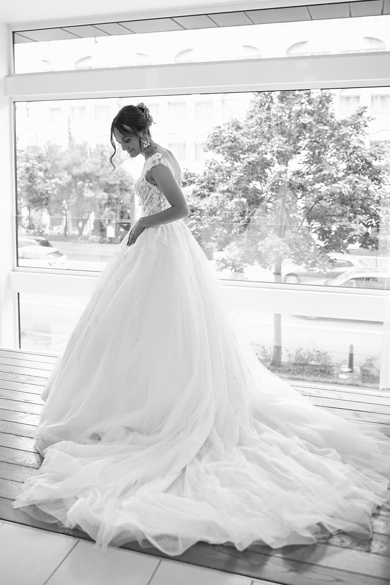 Silhouette of bride in flowing ballgown dress standing by large window.