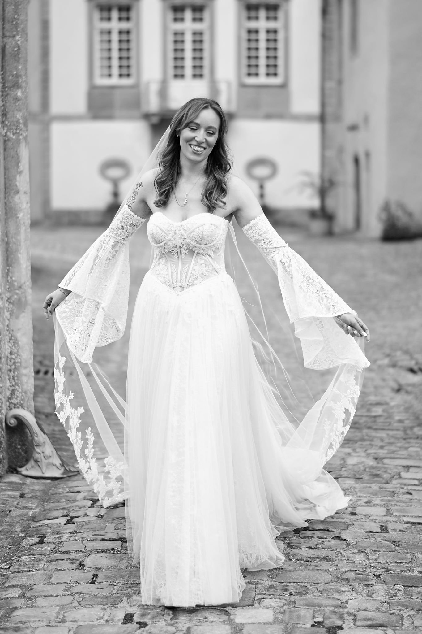 Ethereal bridal portrait on cobblestone path showcasing flowing lace sleeves and full skirt.