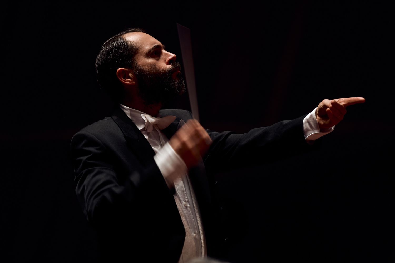 Conductor in formal attire passionately directs orchestra during dramatic performance.