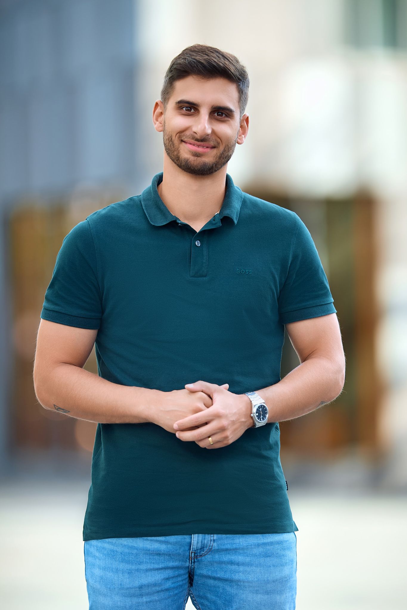 Casual portrait in teal polo shirt and jeans against blurred outdoor background.