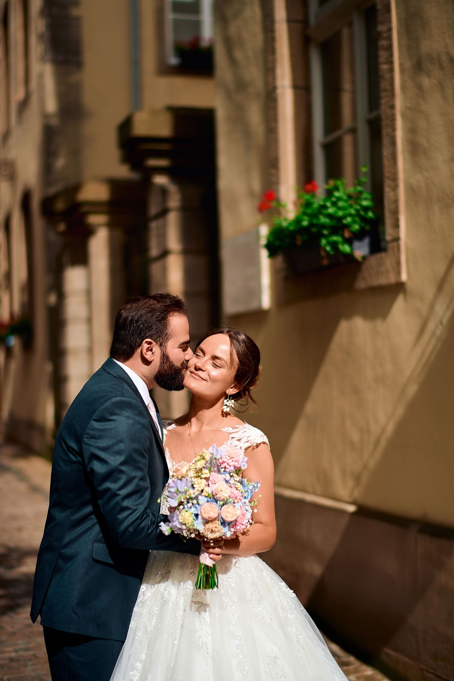 A couple shares a romantic kiss against a stone wall with flower boxes in the background.