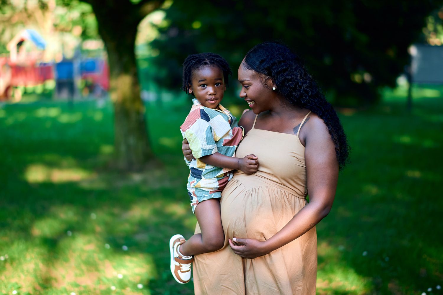 Family maternity photoshoot in a sunny park with green trees.