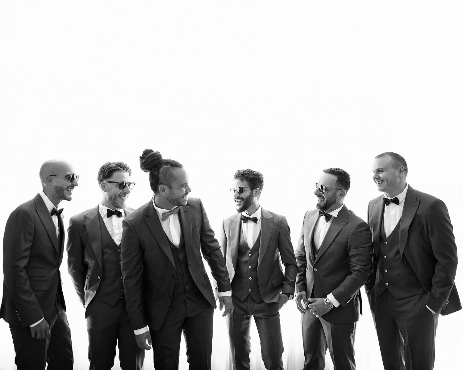 Black and white panoramic portrait of groomsmen lined up in formal suits and bowties.