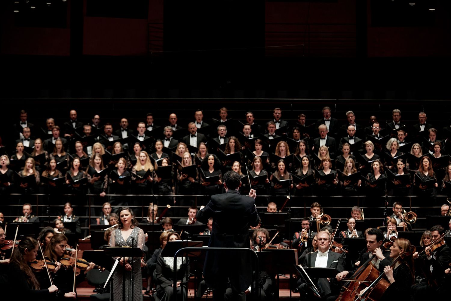 Symphony orchestra and choir performing together on dark stage during classical concert.
