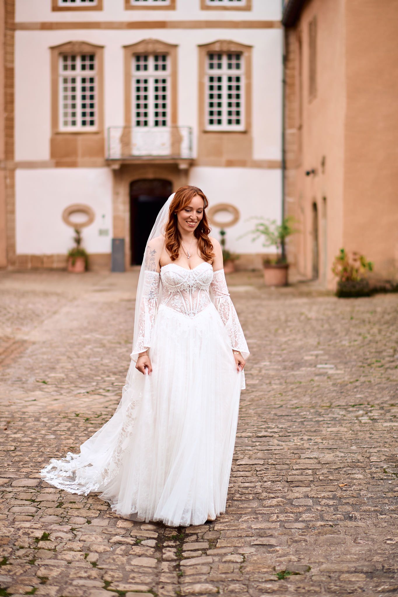 Flowing white wedding dress photographed on cobblestone courtyard with historic building facade.