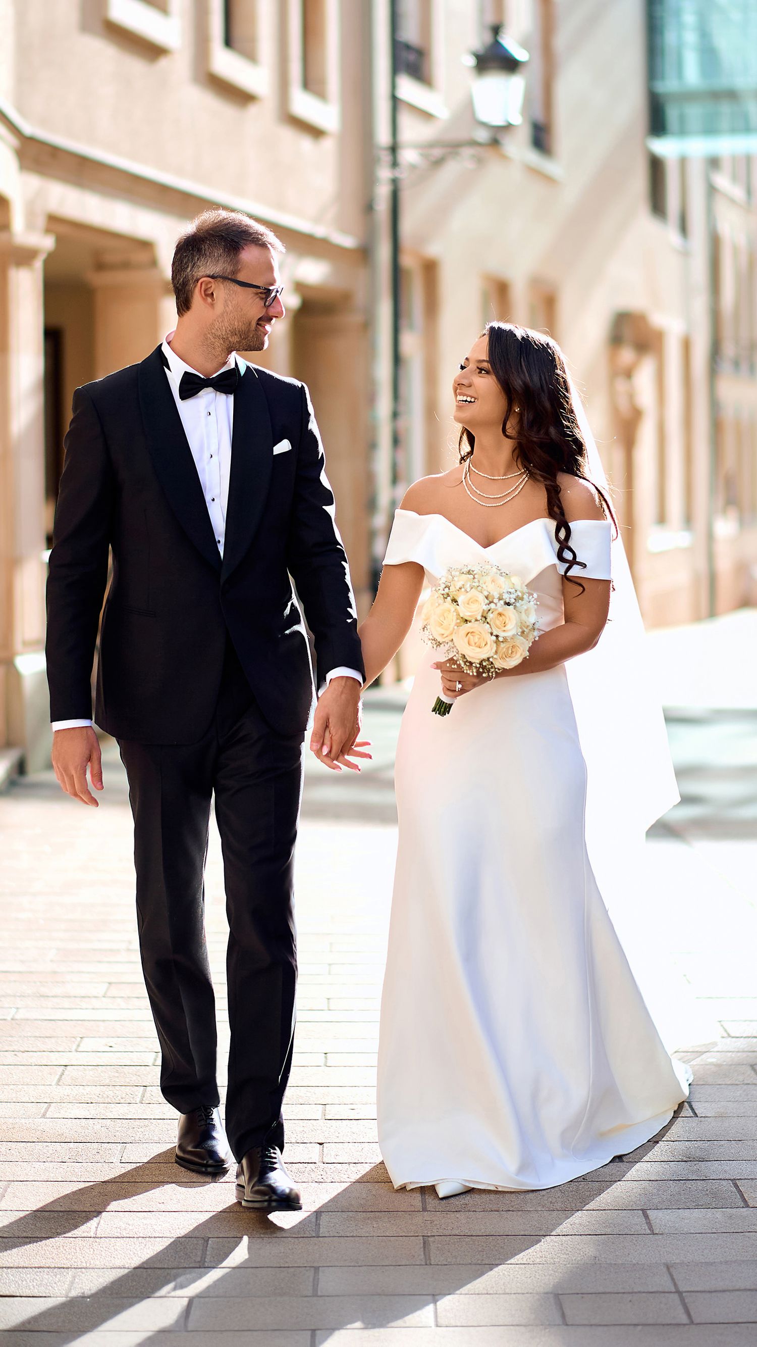 A bride and groom share a joyful moment walking together outdoors in formal wedding attire.