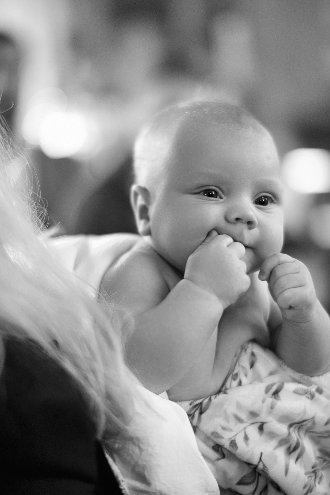 Close-up black and white portrait of infant with hand near mouth.