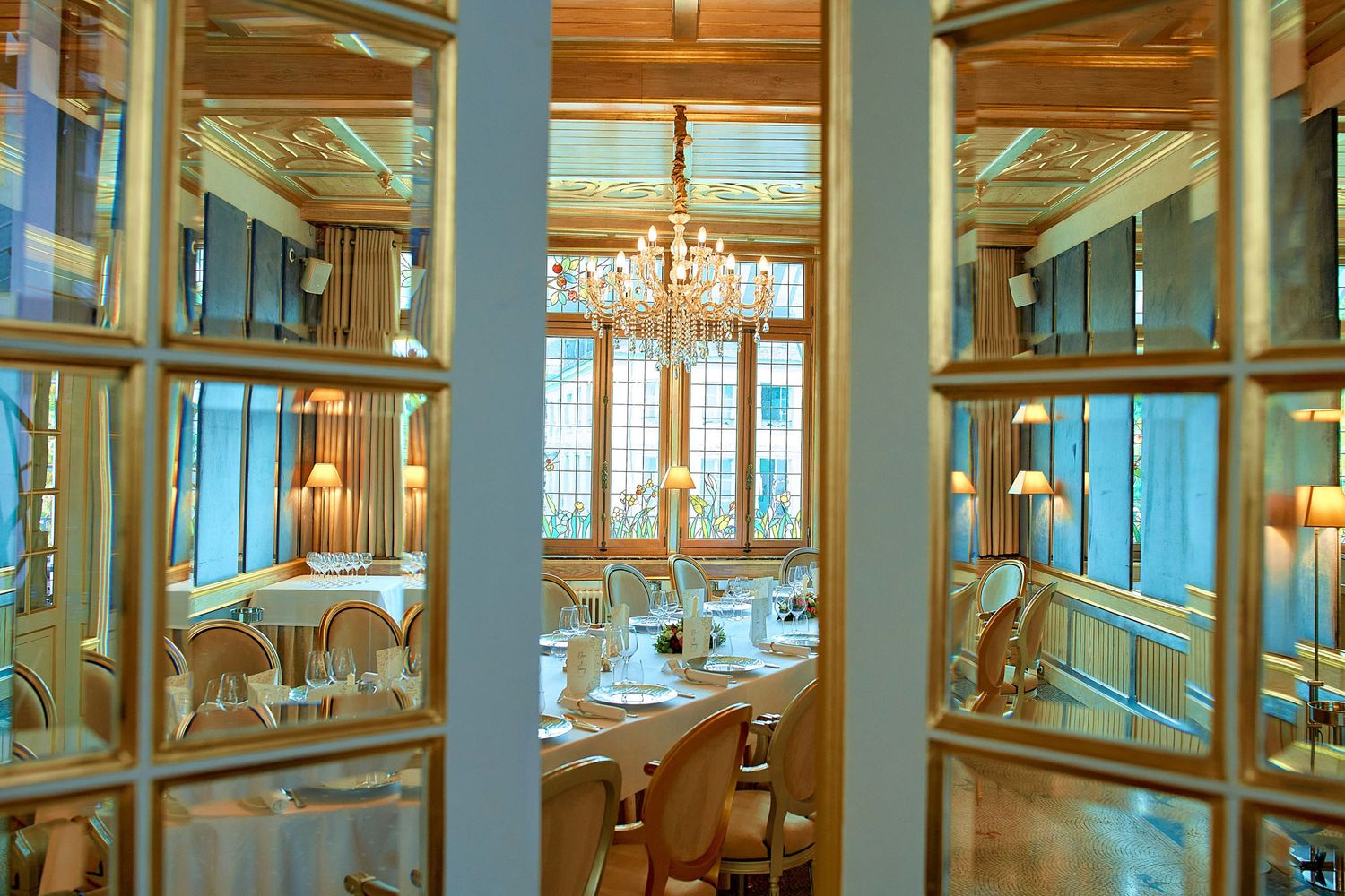 Elegant ballroom interior with crystal chandeliers, wooden paneling and luxurious dining tables set for a formal event.