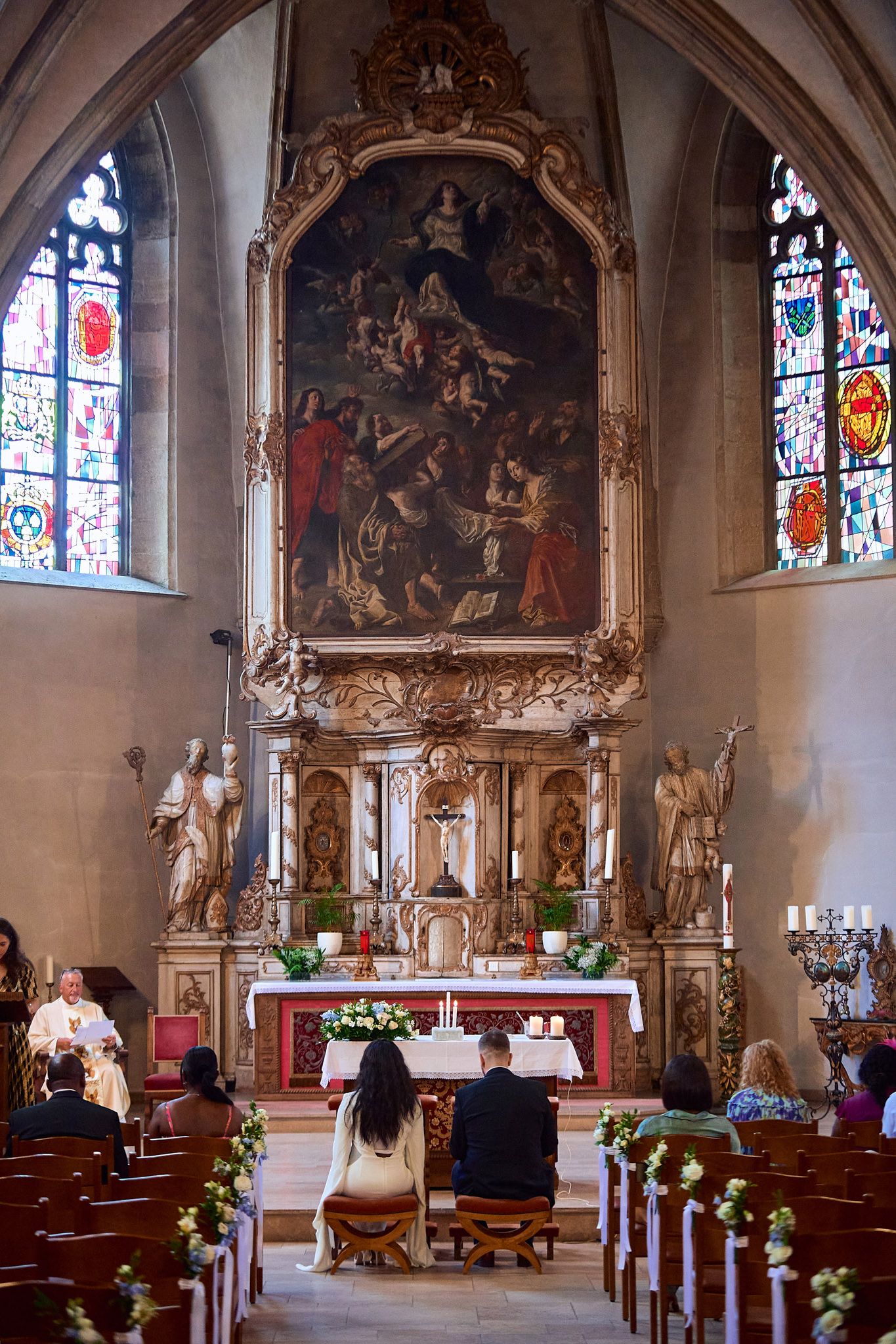 Wedding ceremony setup in historic church with ornate altar painting and stained glass windows.