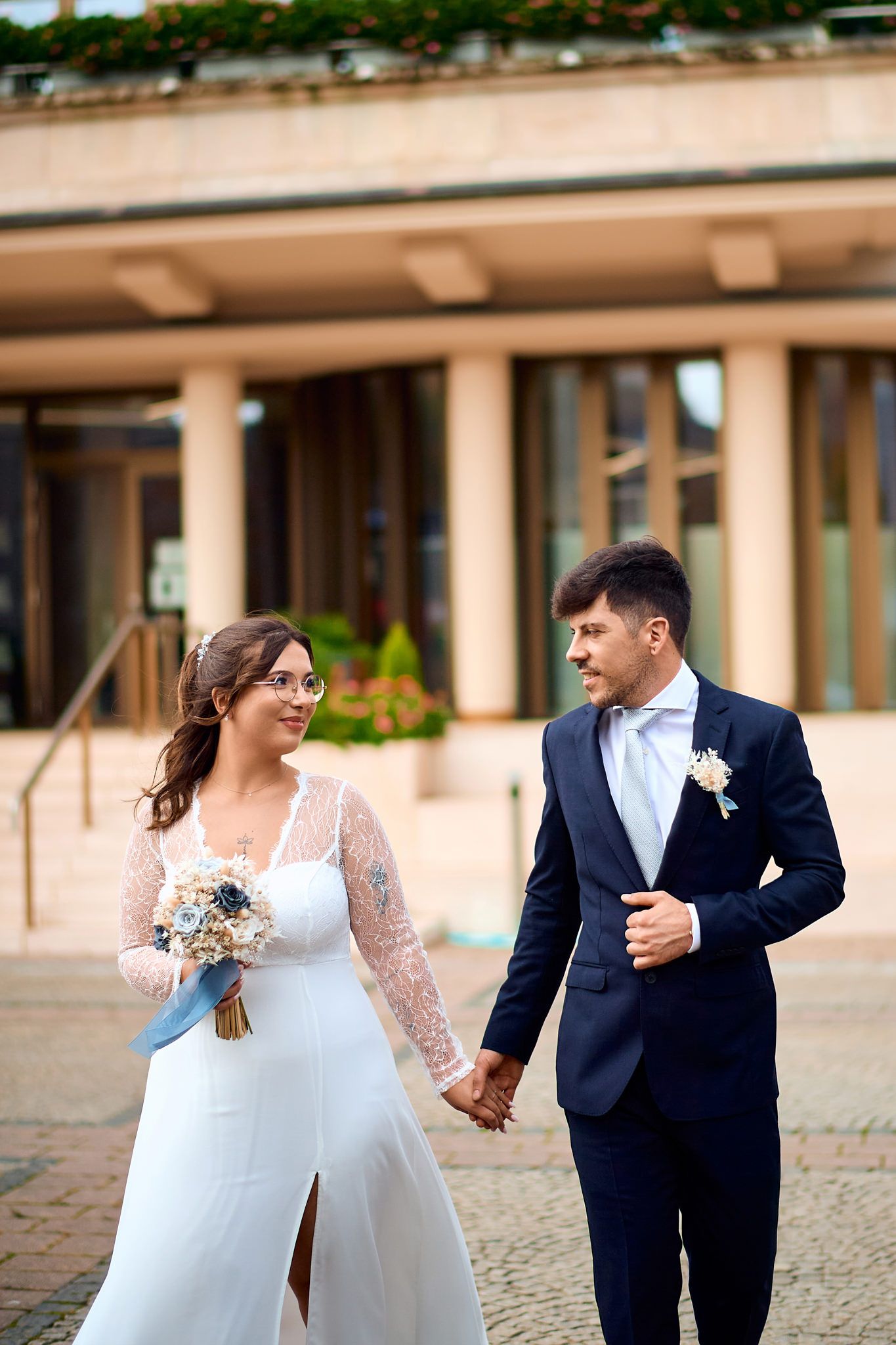 Wedding couple walks together outdoors, bride in white dress and groom in navy suit.