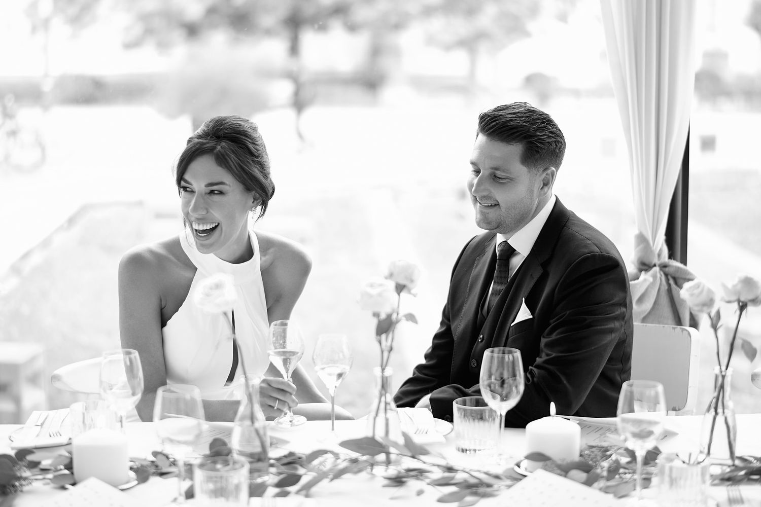 Black and white reception sequence showing couple laughing together at dinner table.