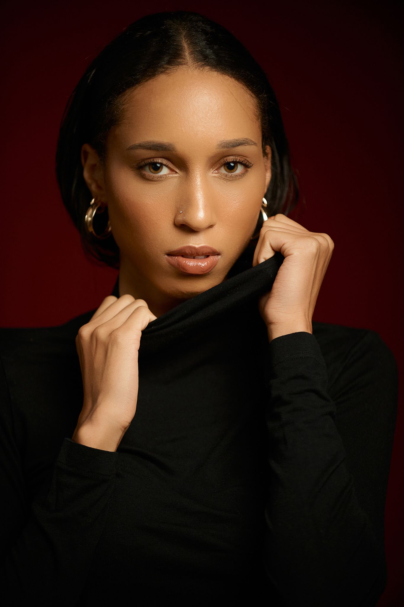 Dramatic close-up portraits against dark red background with black turtleneck.
