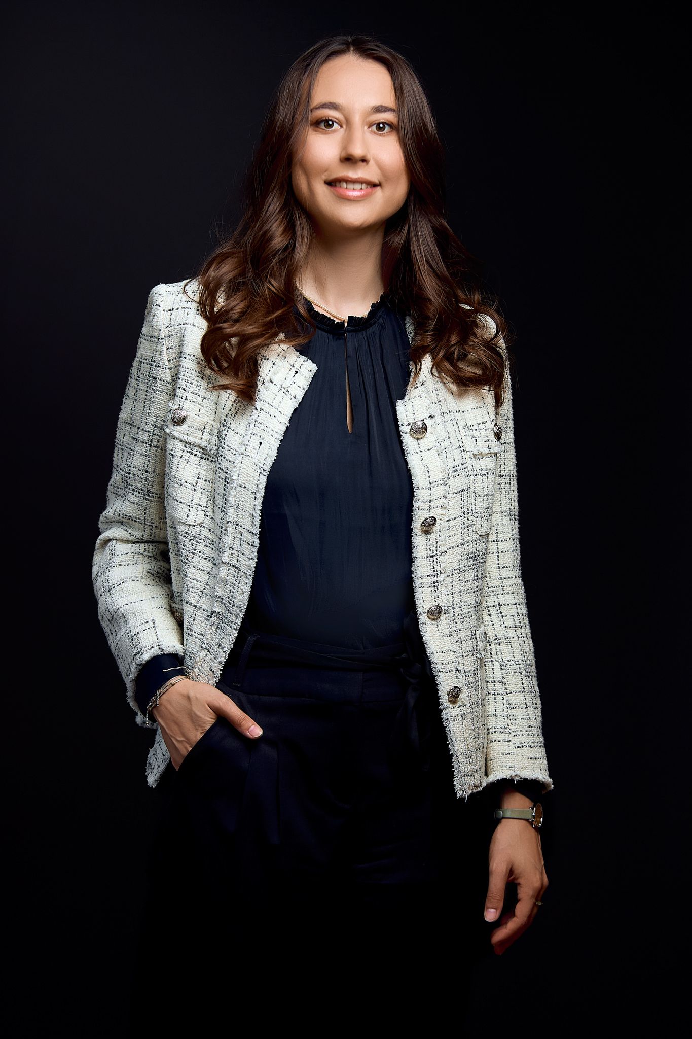 Professional headshot wearing tweed blazer and navy blouse against black background.