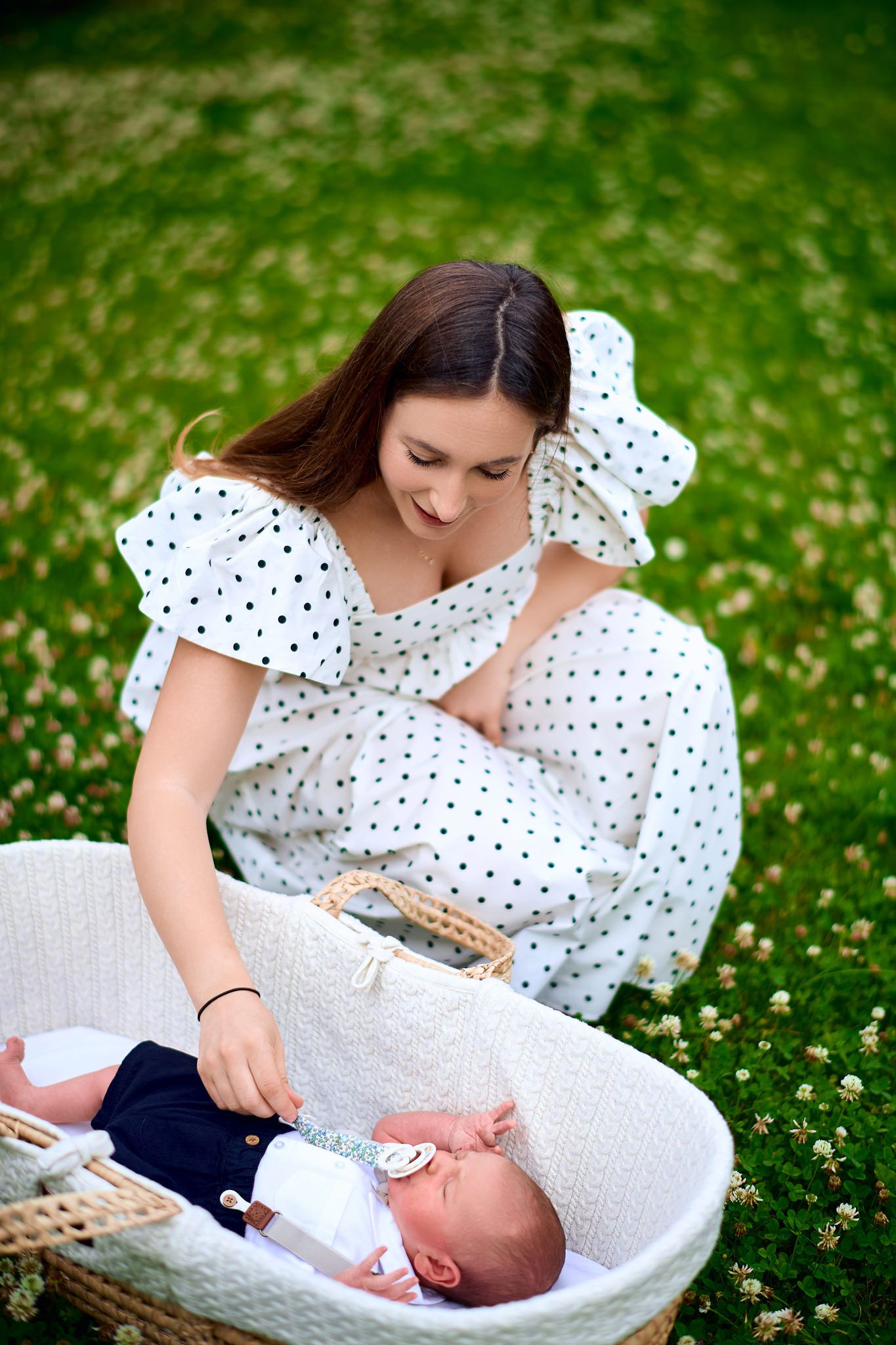 Parents tending to their baby in a cozy woven basket on a grassy field.