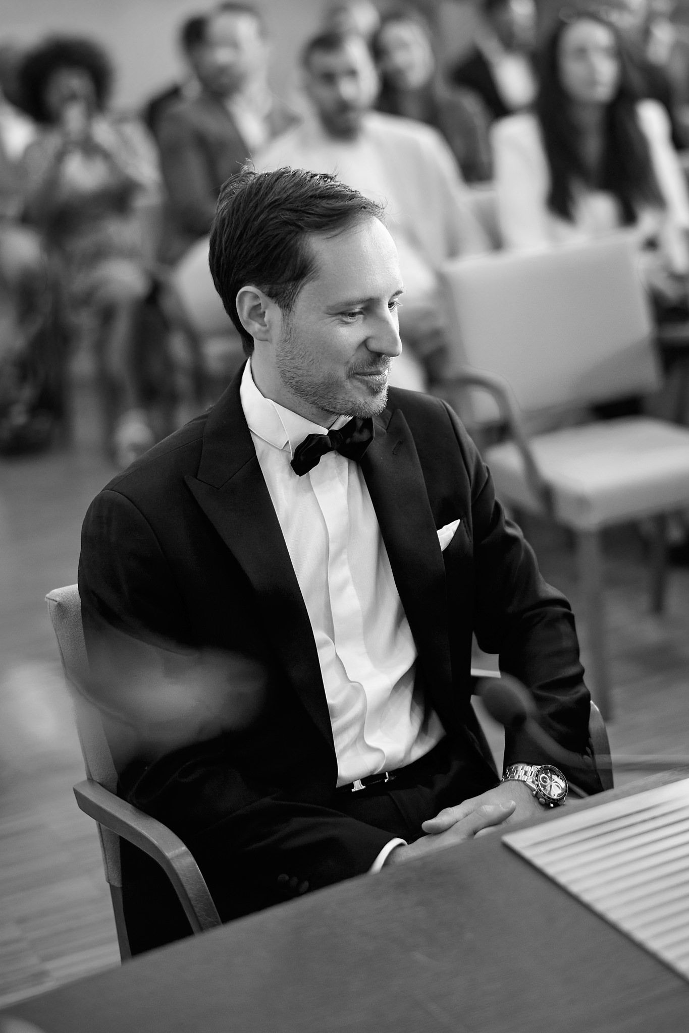 A person in formal attire sits thoughtfully in black and white.