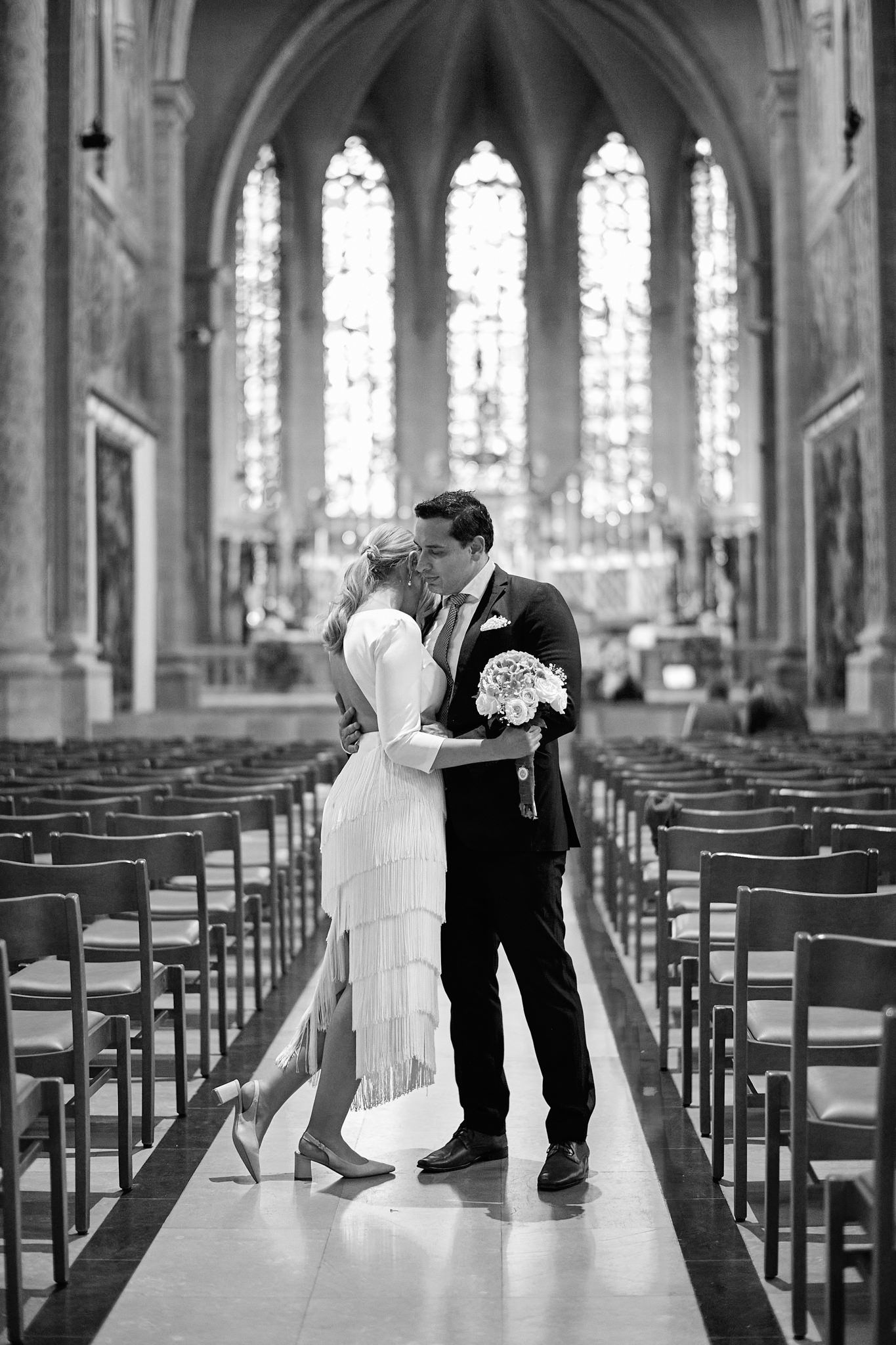 A couple shares a romantic moment in a grand cathedral with rows of empty chairs and gothic architecture.