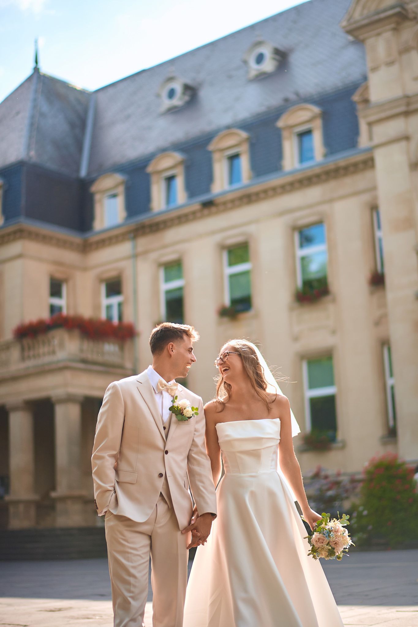 Wedding couple shares joyful moments outside an elegant stone building in warm sunlight.