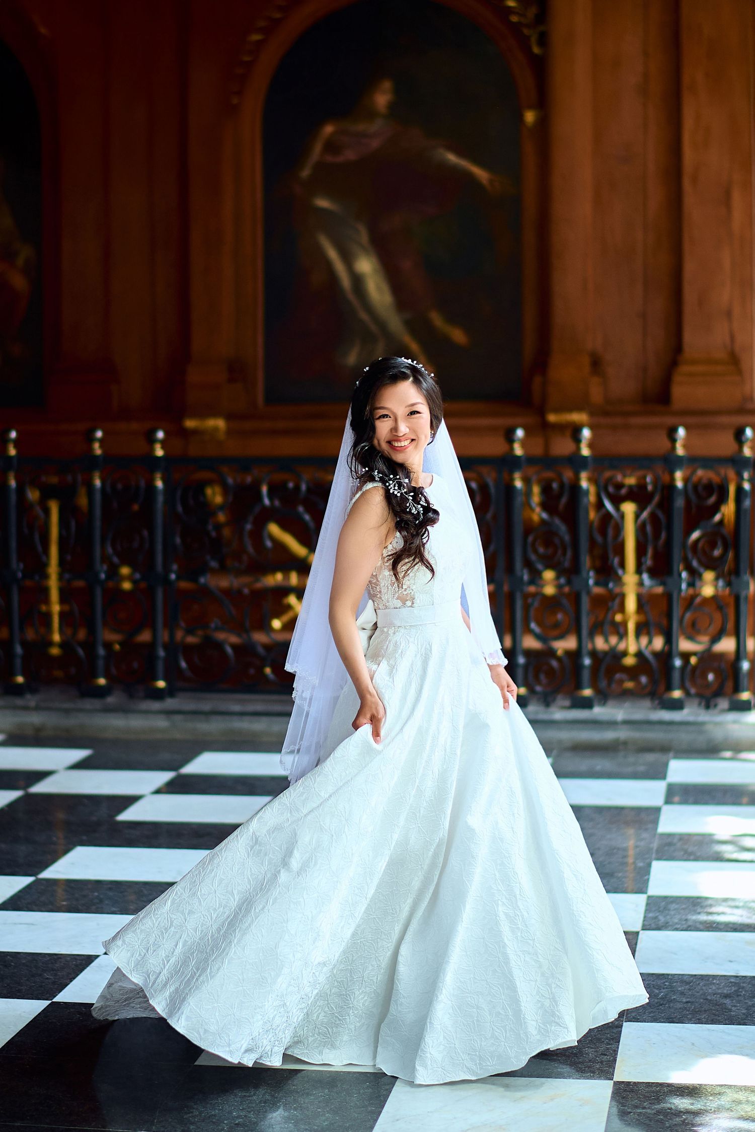 Bride spins in flowing white wedding gown on checkerboard floor.