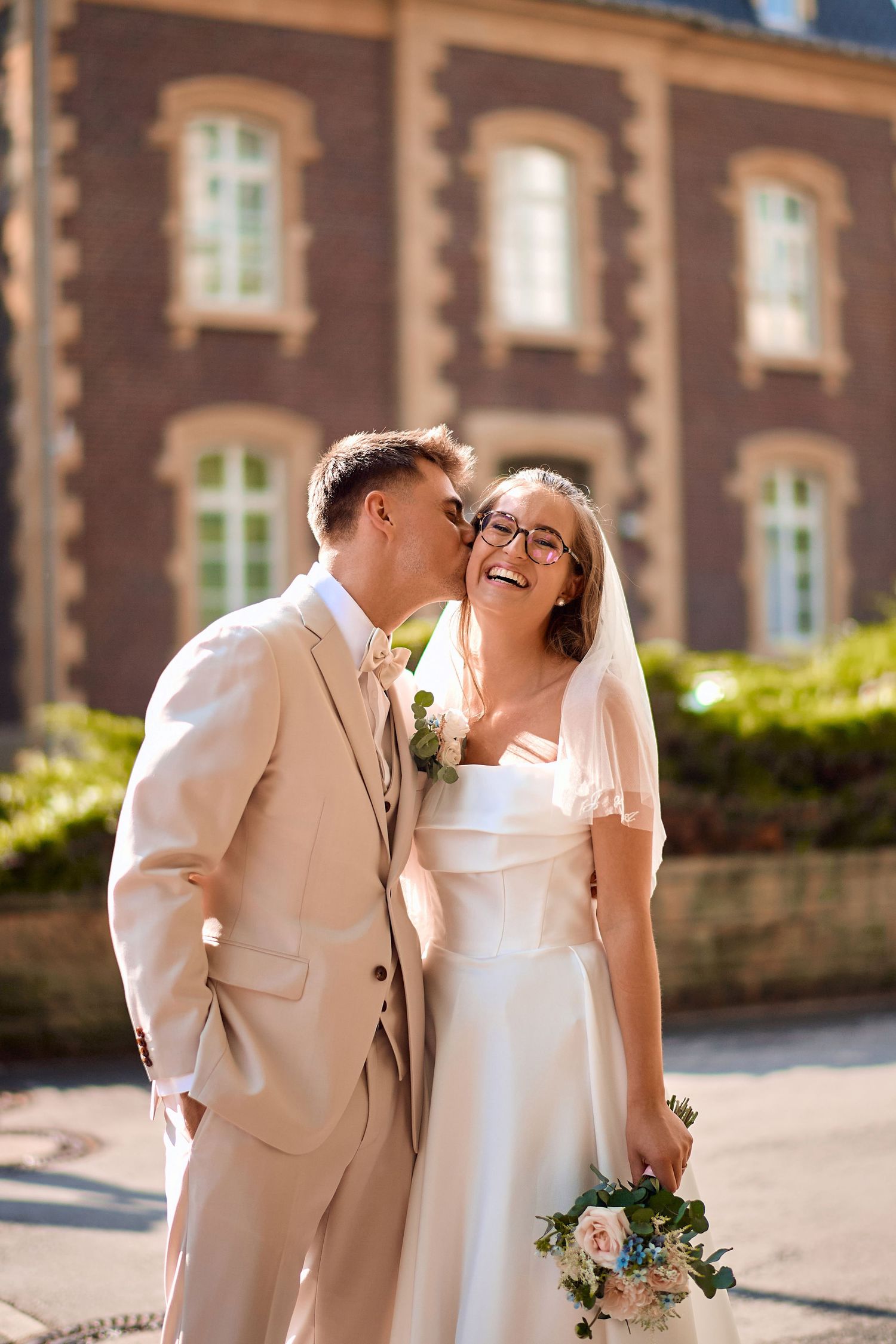 Joyful wedding couple sharing intimate moment outside historic building.