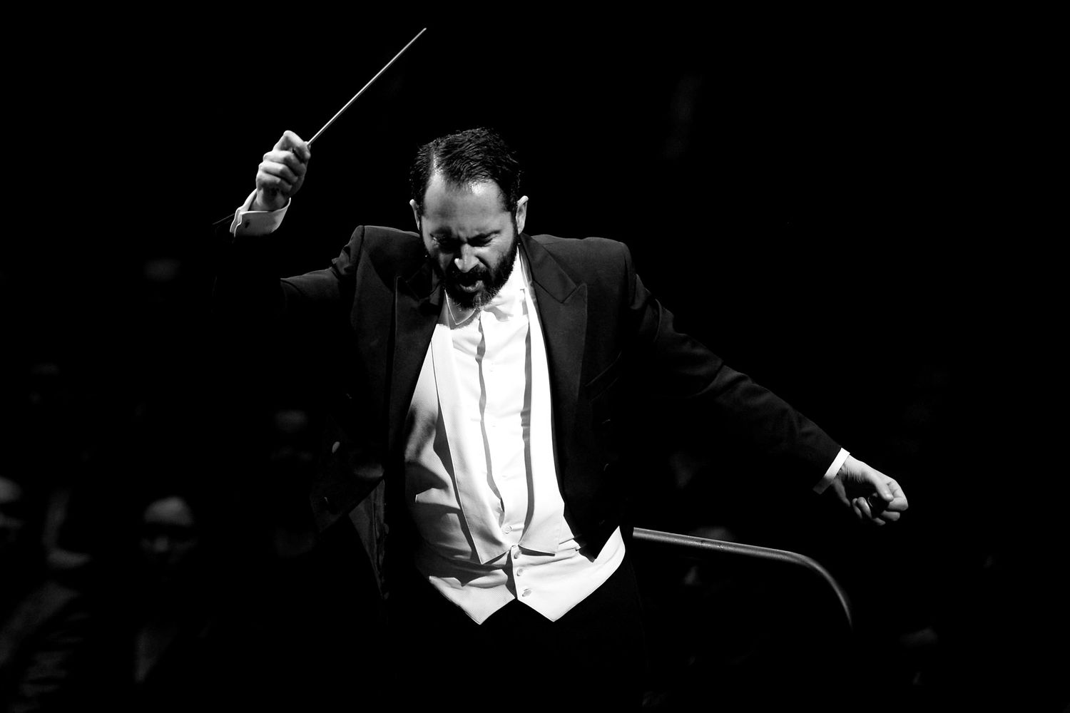 Orchestra conductor in white tie dress leads performance with expressive hand movements.