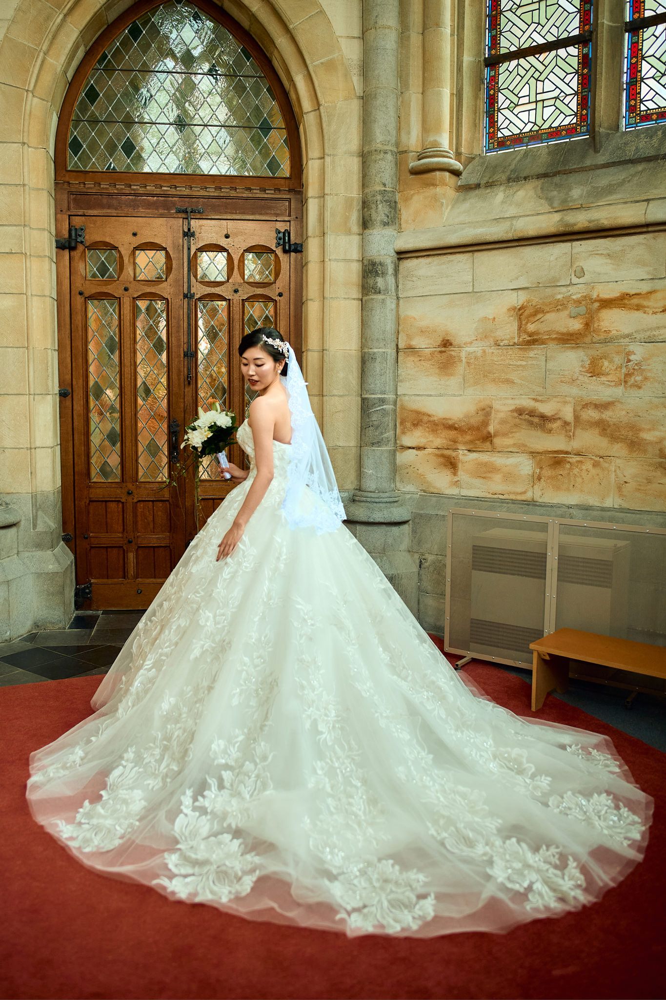Stunning bridal gown with intricate lace details and cathedral train photographed in church setting.