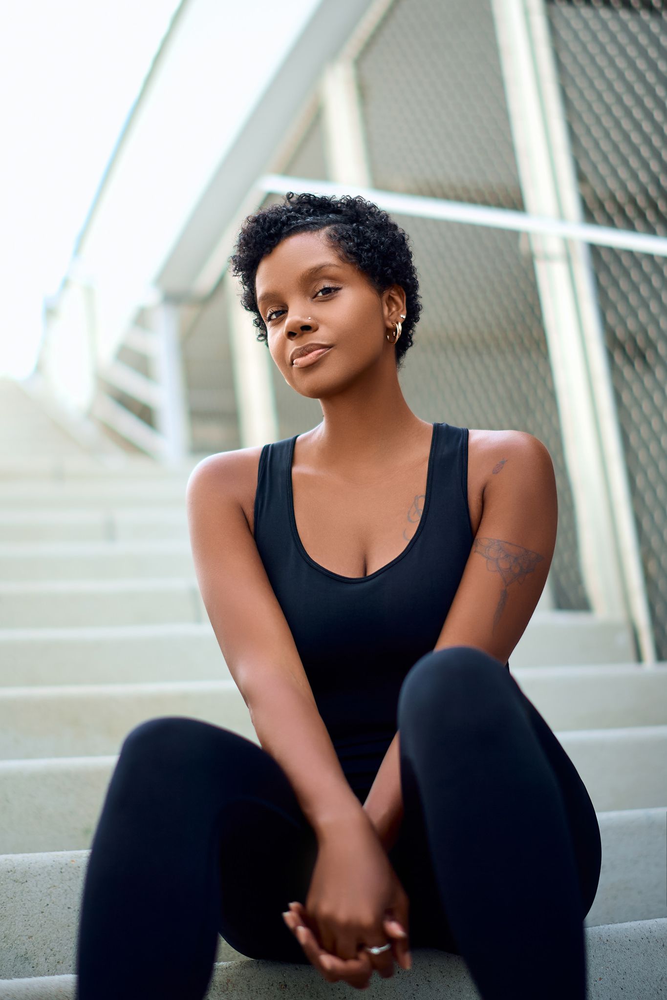 Athletic figure in black workout attire poses on concrete steps during an outdoor fitness photoshoot.