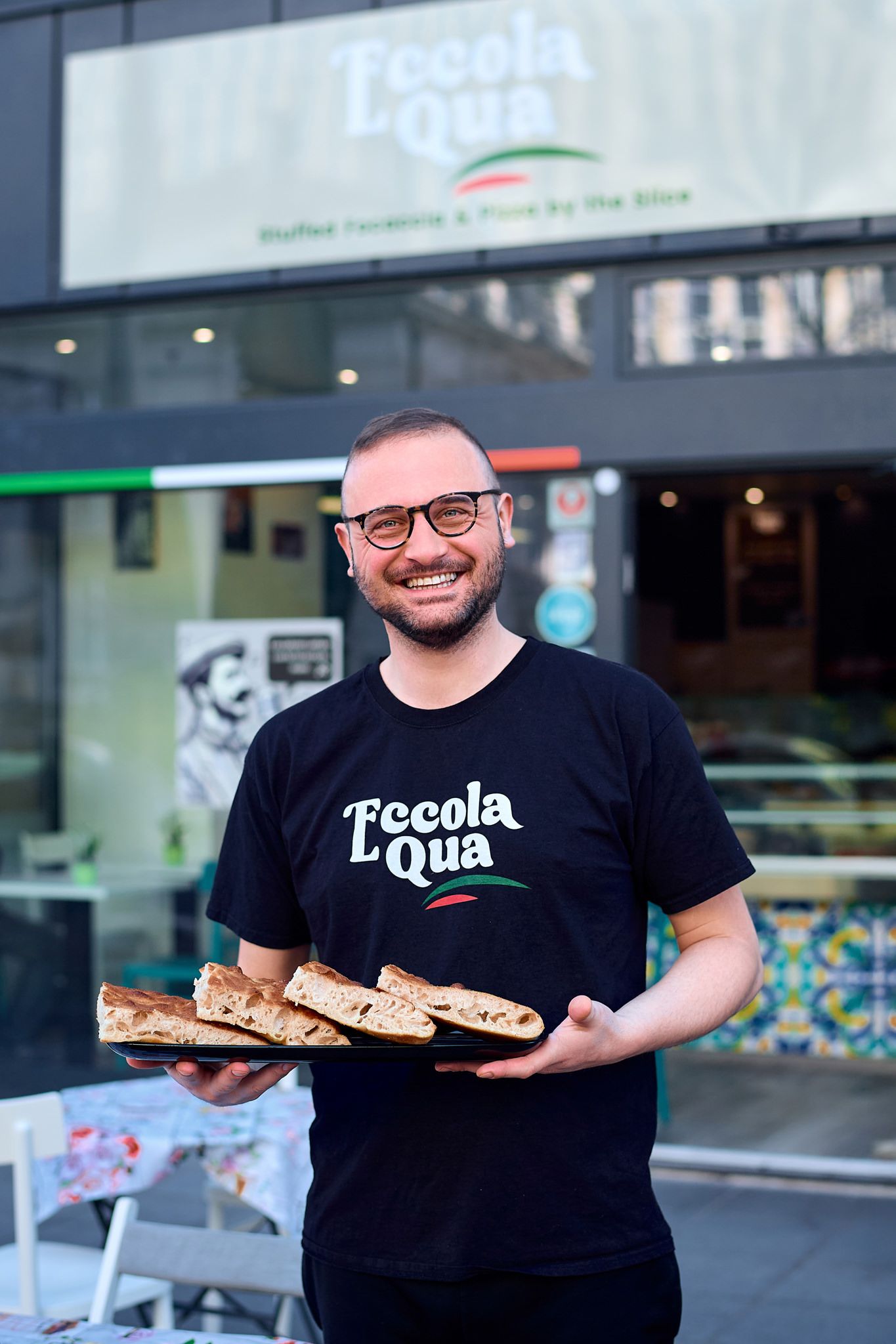 Food service worker displaying sandwiches outside restaurant storefront.