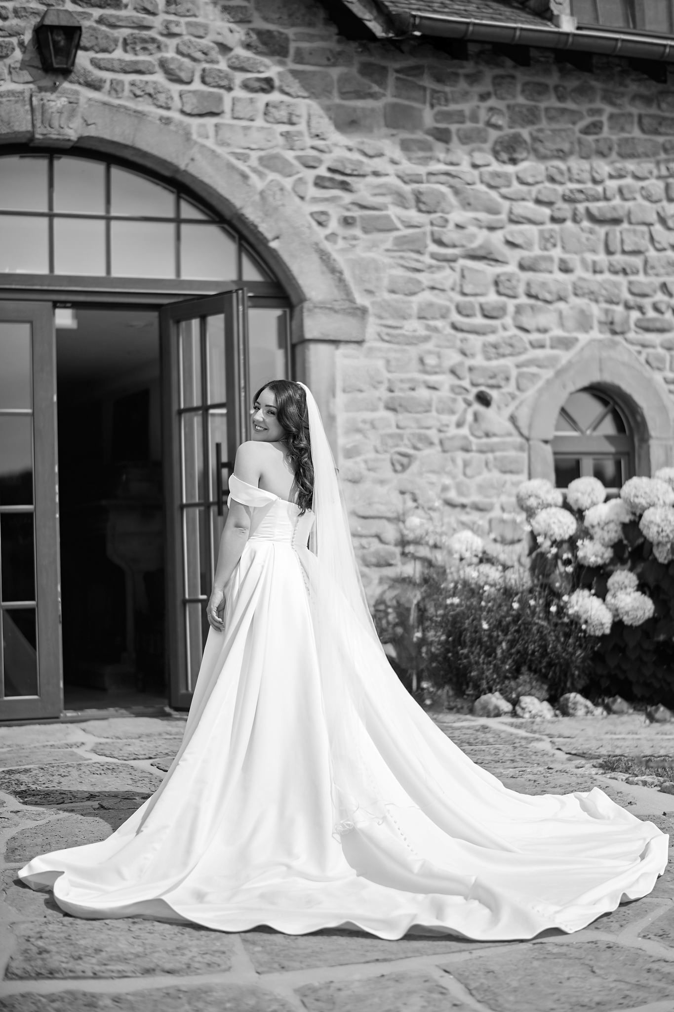 Wedding dress train elegantly displayed against rustic stone wall in black and white sequence.
