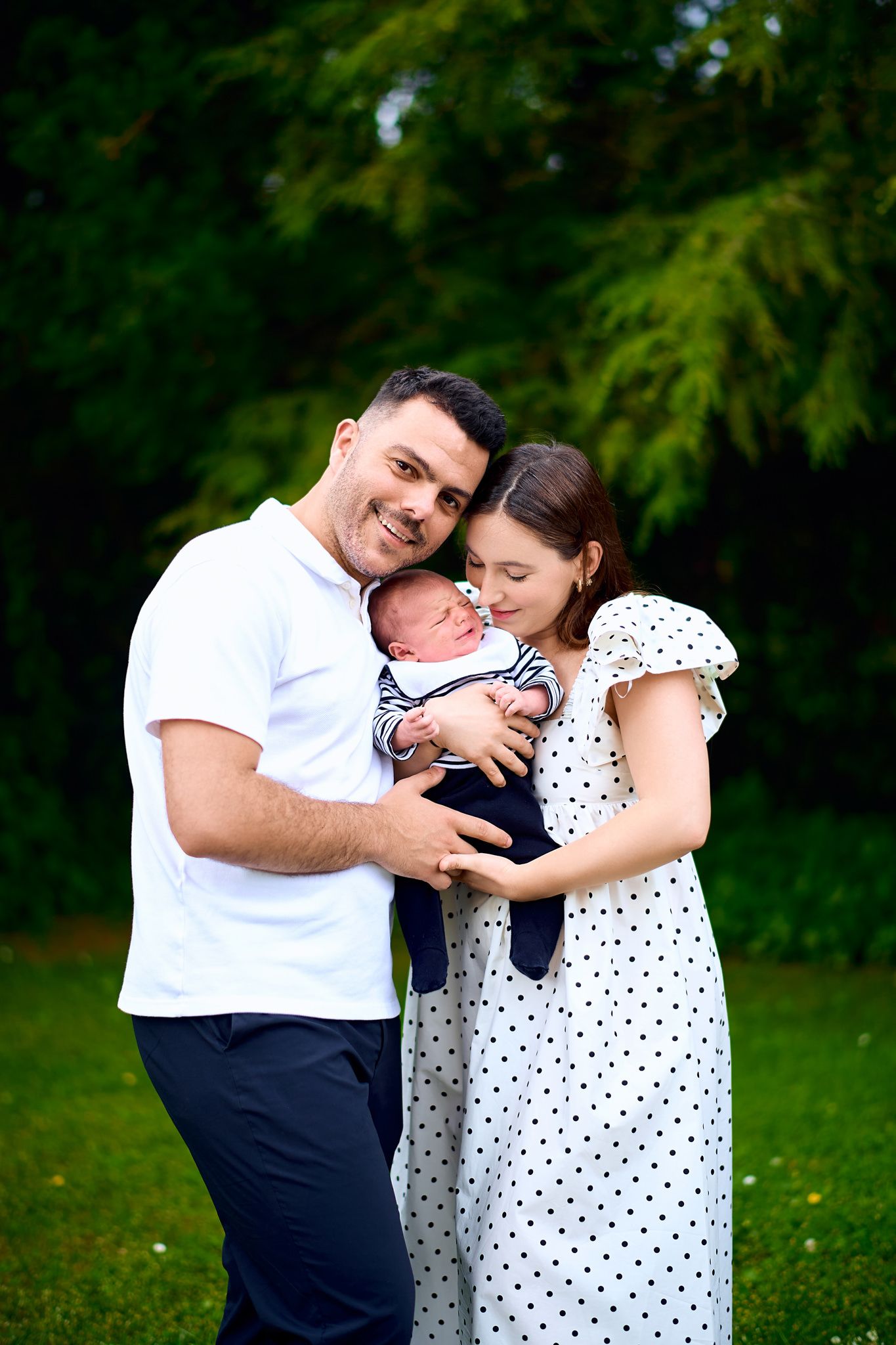Family portrait session in a garden setting with coordinated navy and white polka dot outfits.