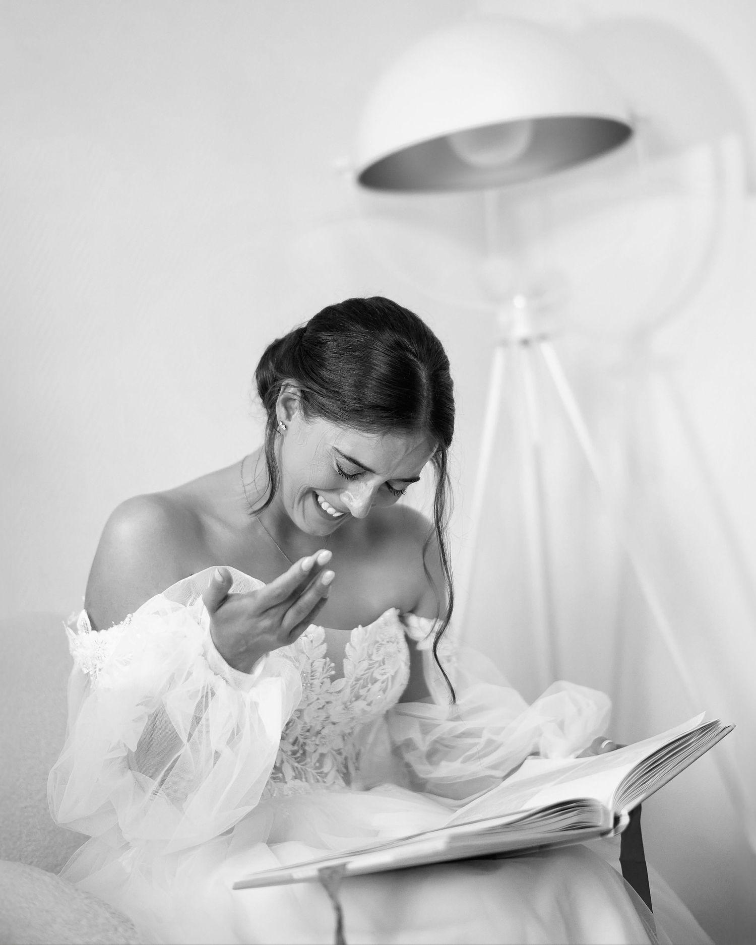 A bride in a lace gown reads emotionally from a book while sitting in soft lighting.
