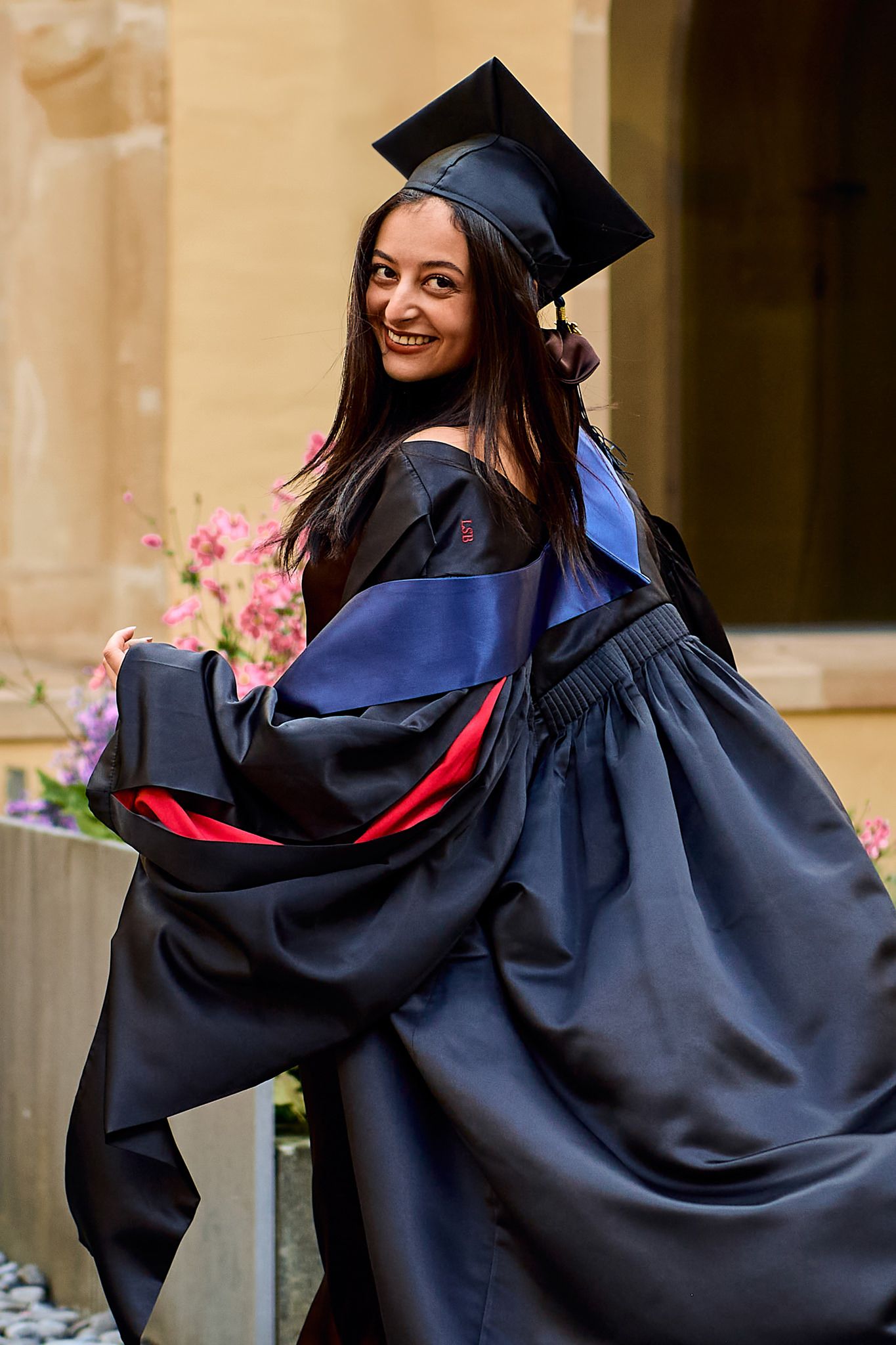 Graduate in traditional cap and gown poses playfully during graduation photoshoot.