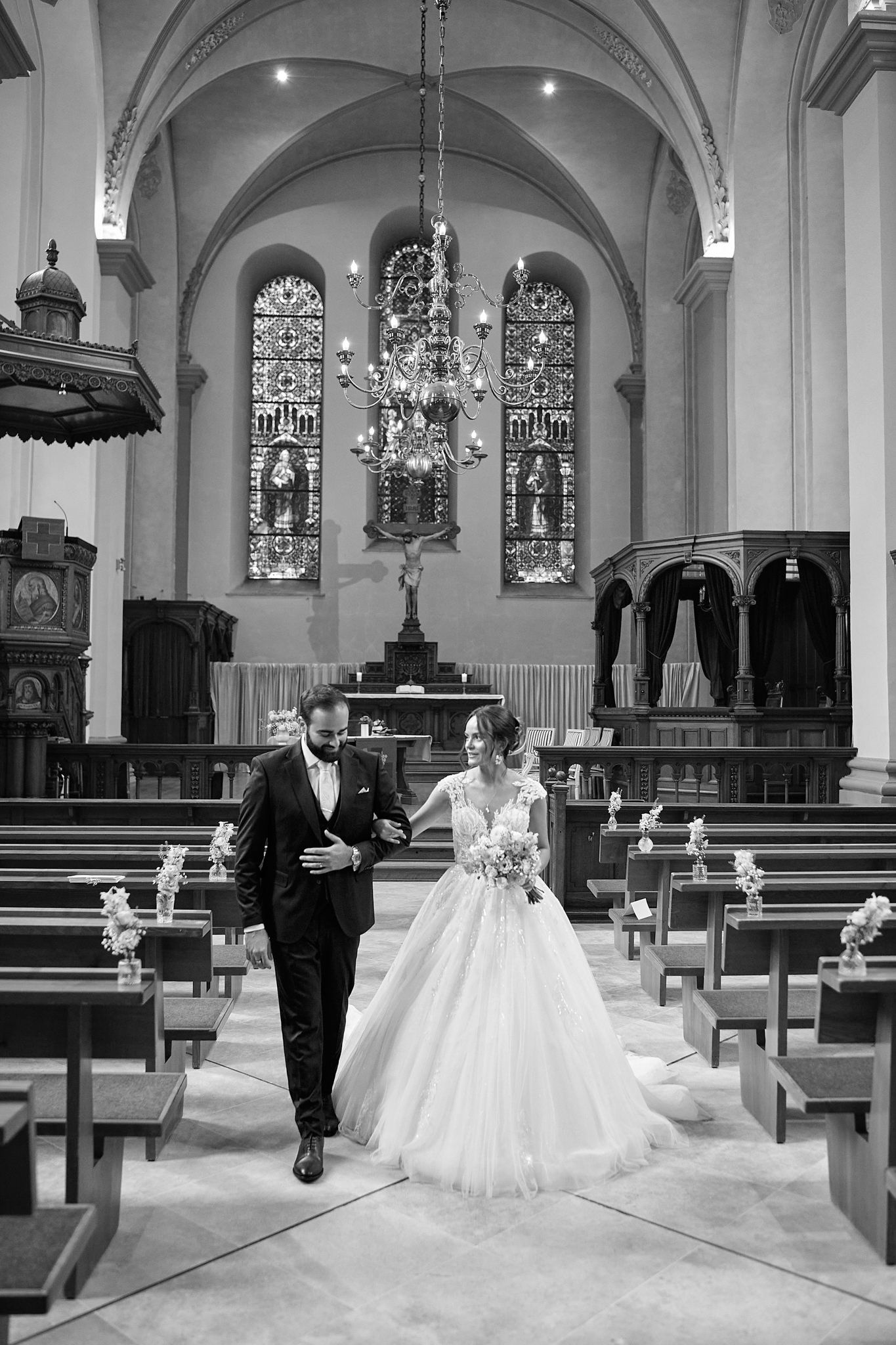 A black and white photograph of a wedding ceremony in a grand church with stained glass windows.