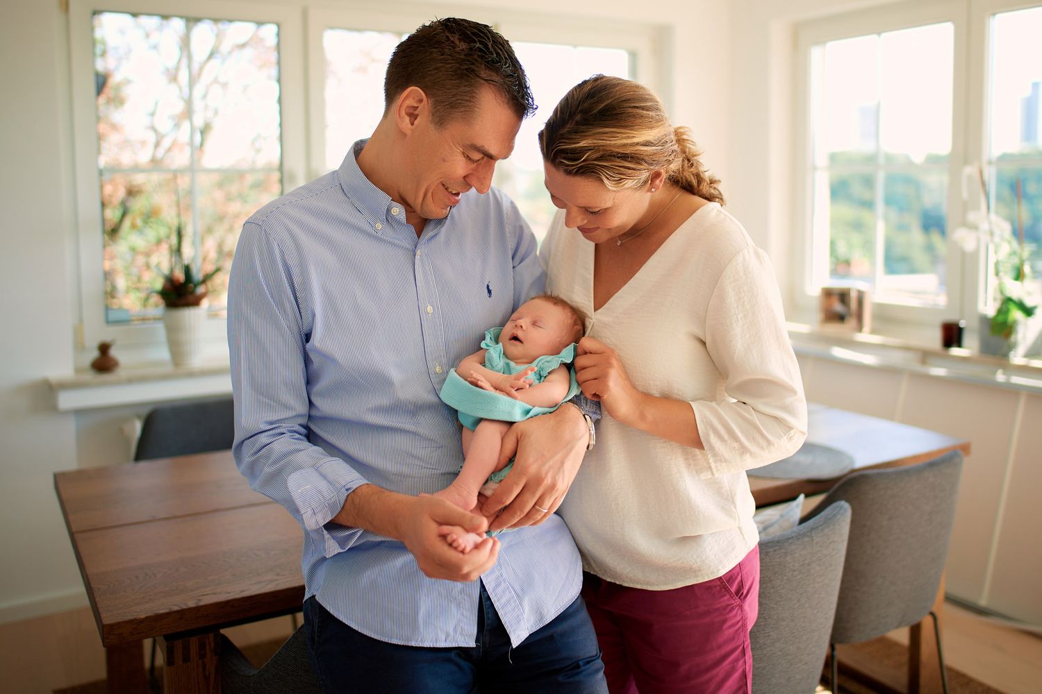 Parents share intimate moments with newborn in bright sunlit room.