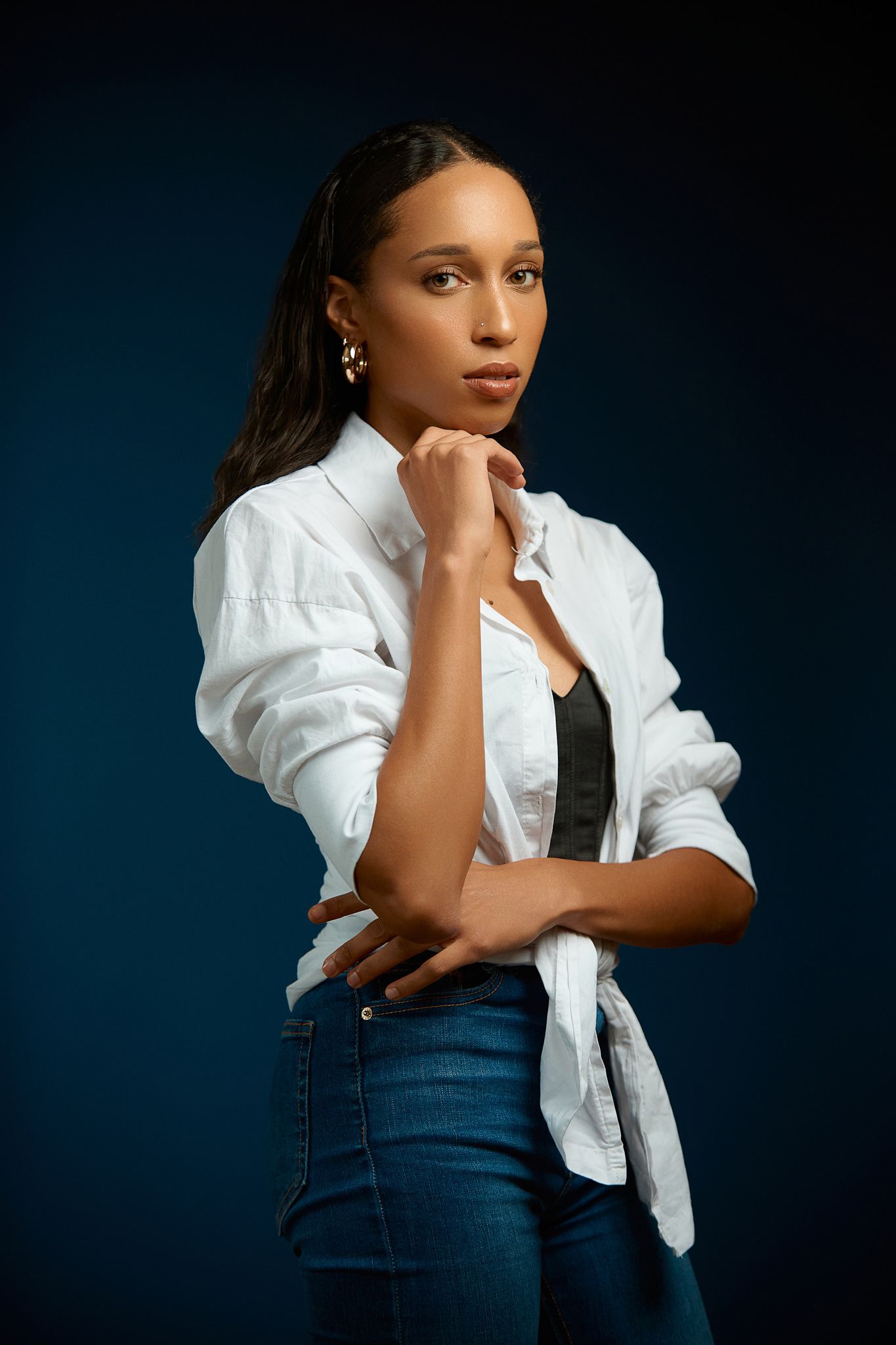 Professional portrait series in white puffy sleeve top and denim against dark background.