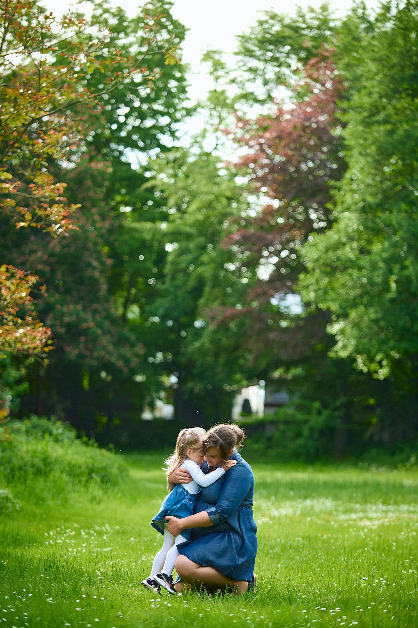Intimate family moment captured in lush green garden setting with white flowers.