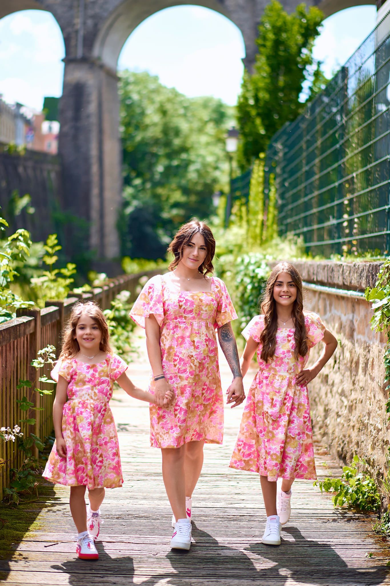 Three children in matching pink floral dresses playing on a stone walkway.