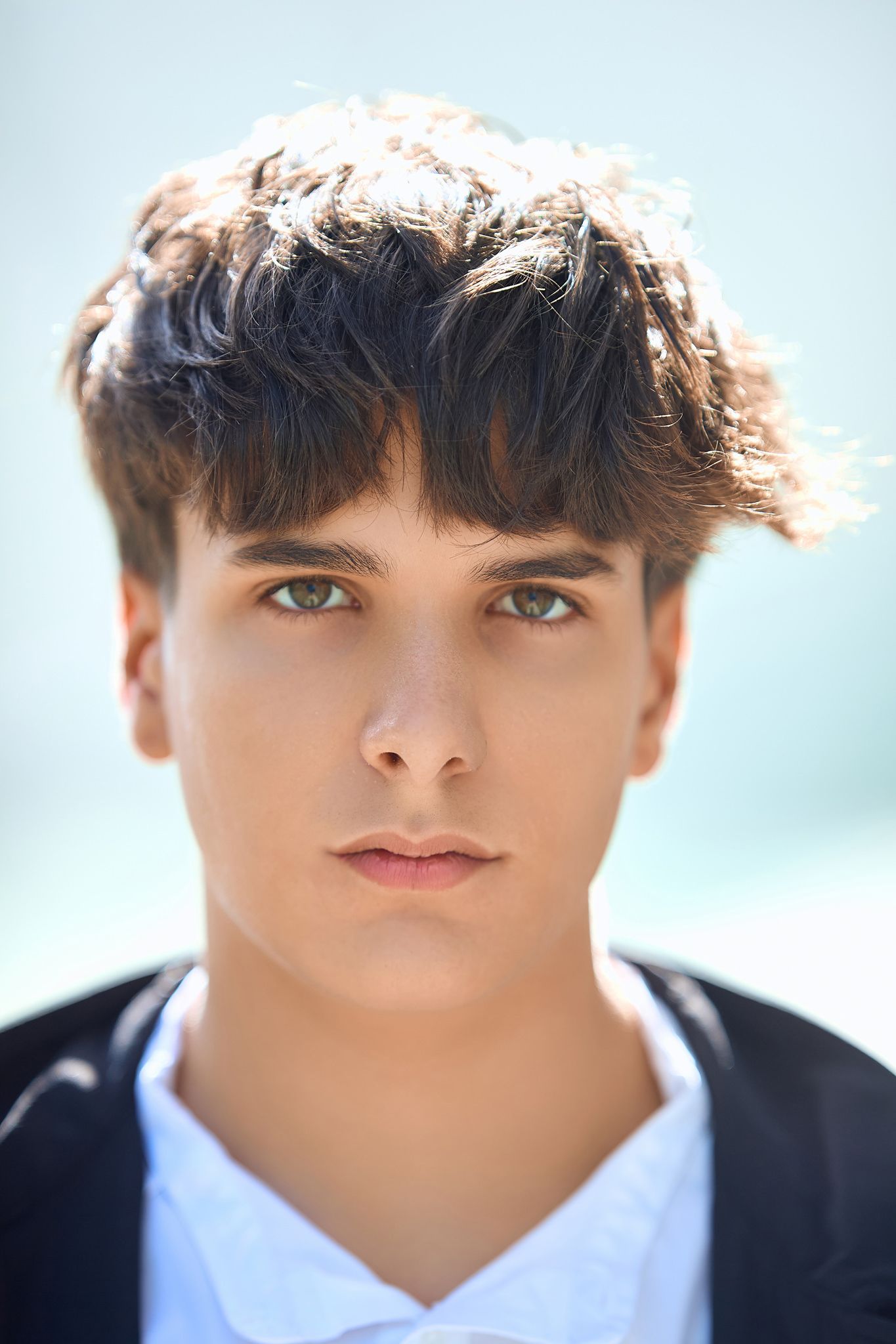 Close-up portrait shot against a light blue background showing dark hair and white collar.