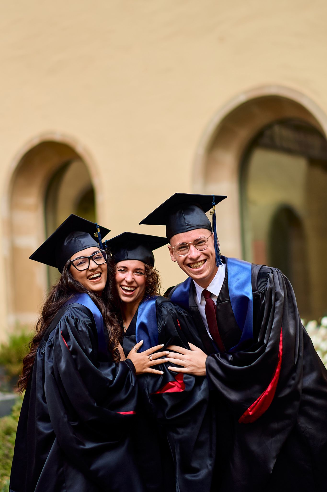 Graduates in black gowns and caps share joyful embraces during commencement.