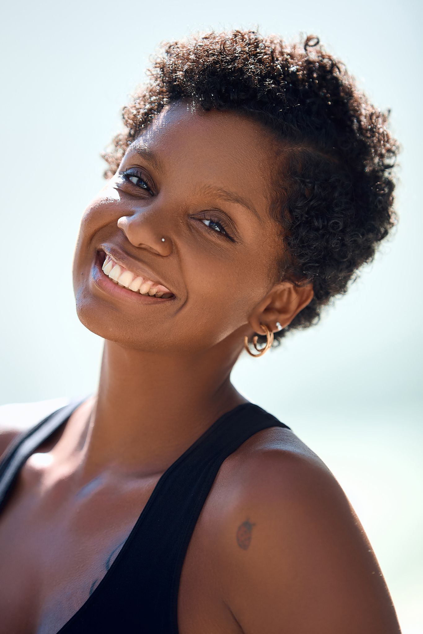 Close-up portrait with natural curls and joyful expression against light background.